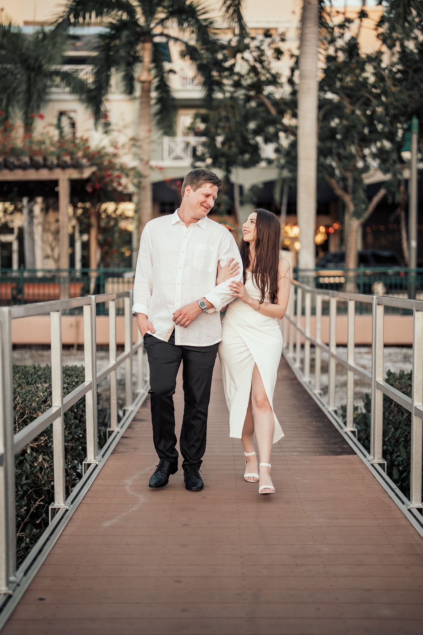 A happy couple walks arm in arm on a wooden bridge surrounded by lush tropical greenery.