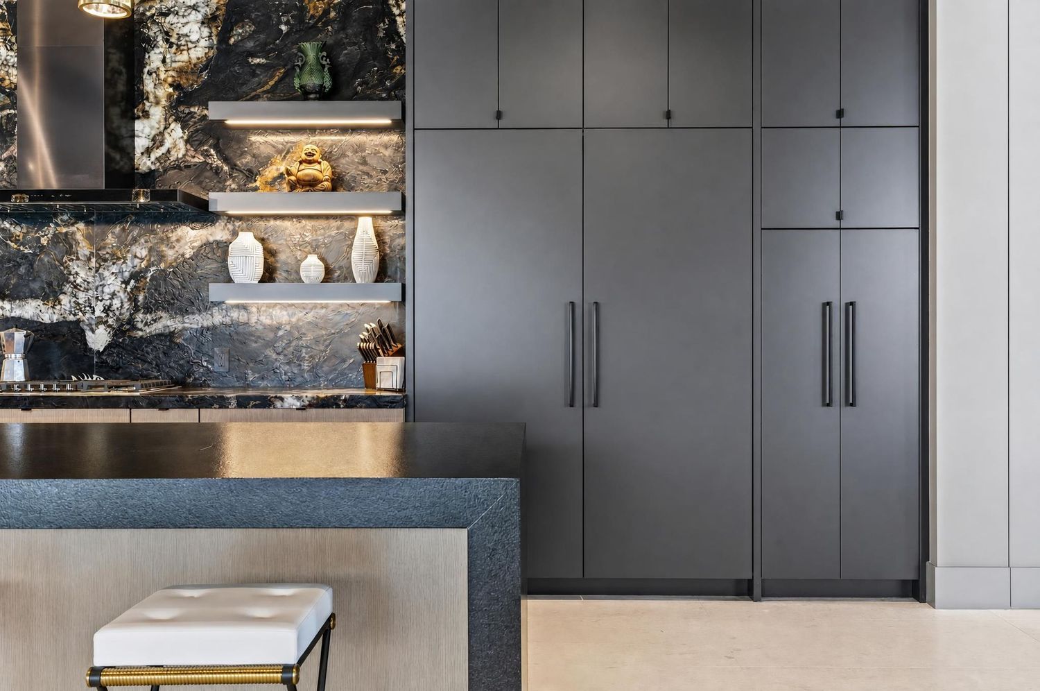 Modern dark gray kitchen cabinetry with marble backsplash, open shelving, and white upholstered bar stool.