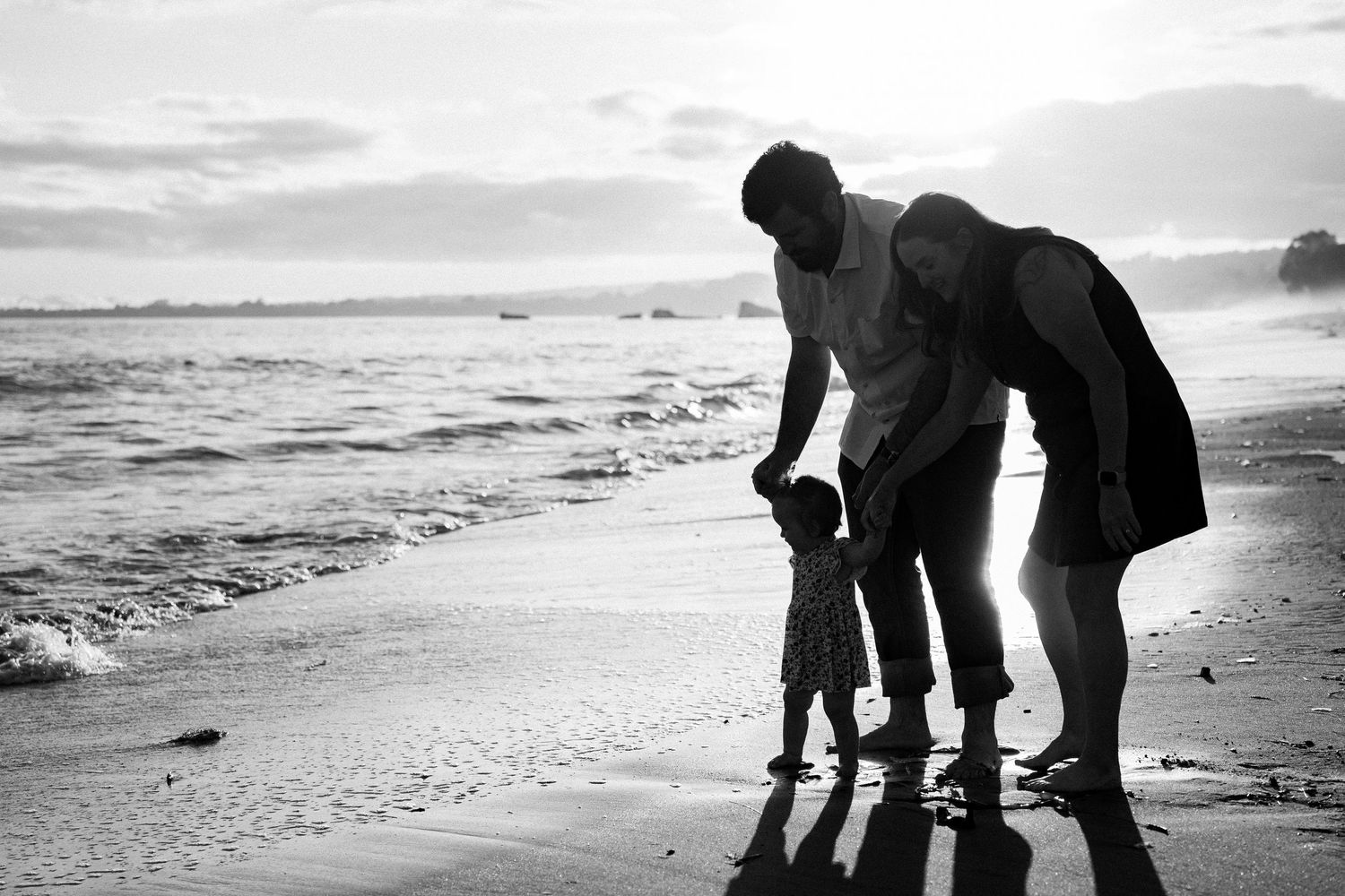 Black and white silhouette of family with young child walking on beach at sunset.