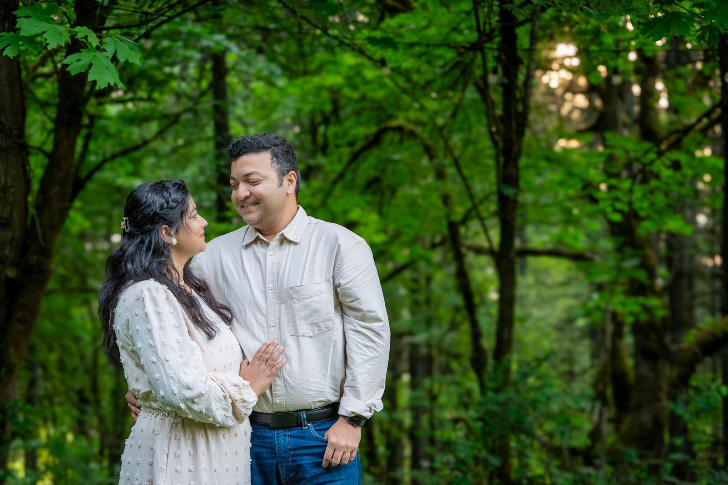 Couple smiling at each other among lush green trees during a relaxed outdoor couples photography session