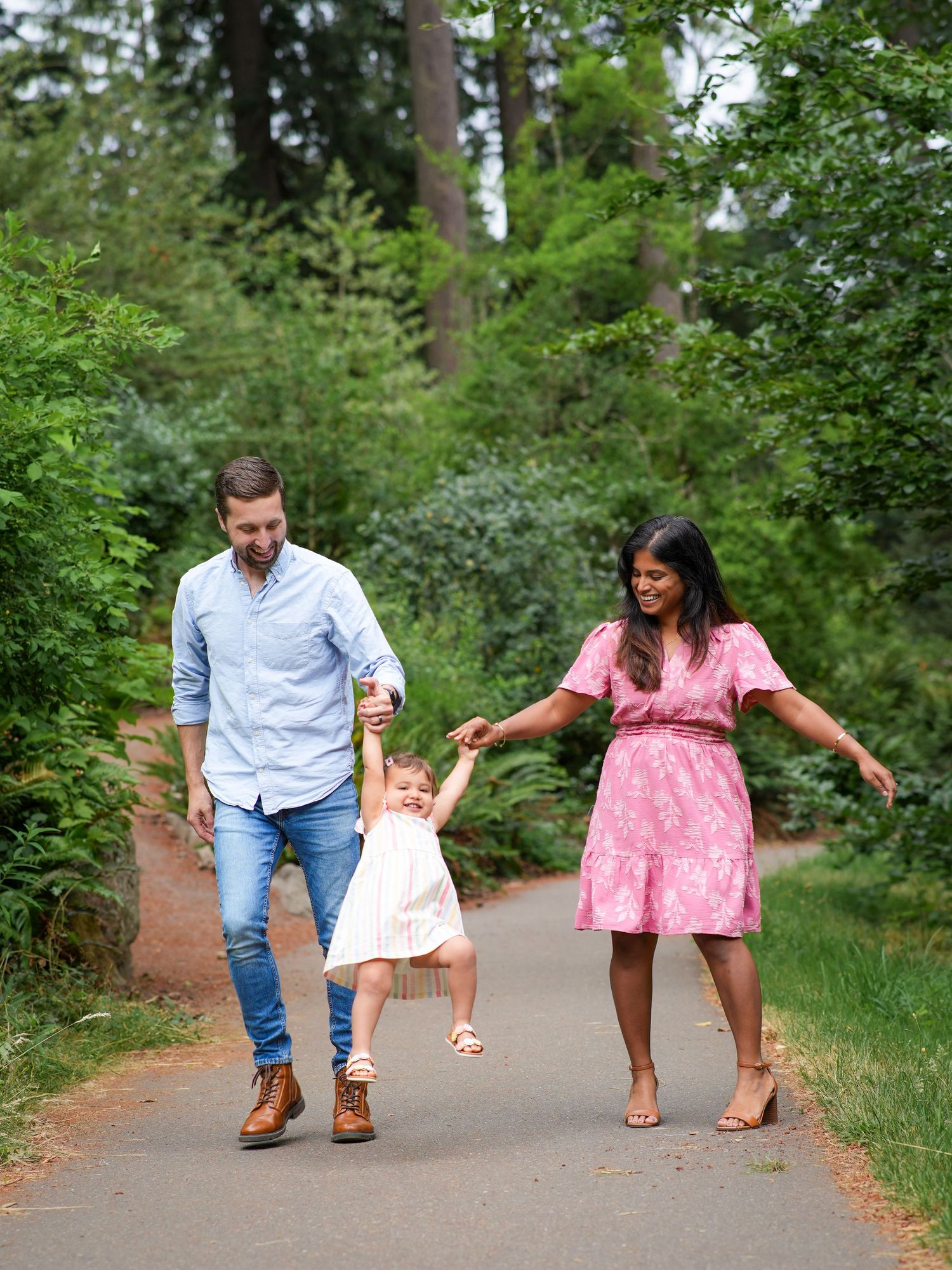 Parents laughing as they swing their toddler between them during a playful outdoor family photography session