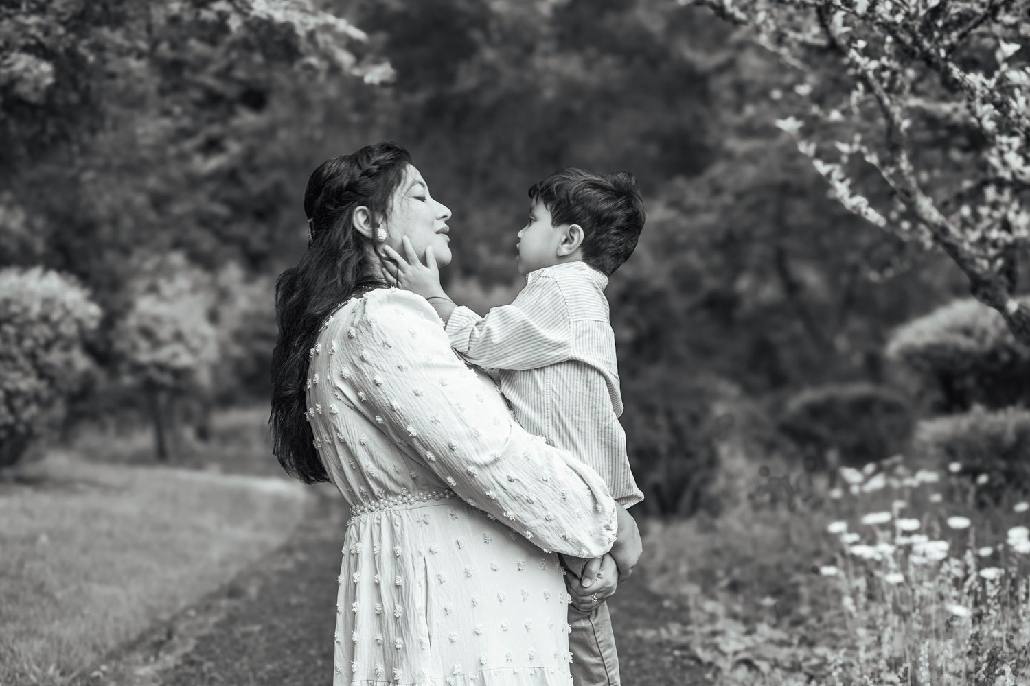 Black-and-white portrait of a mother smiling at her young son while holding him outdoors.