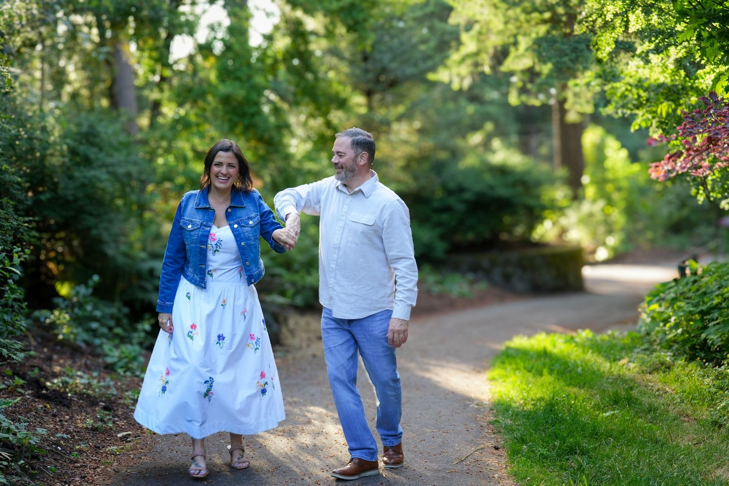 Couple laughing and holding hands while walking through a lush garden during an outdoor photography session