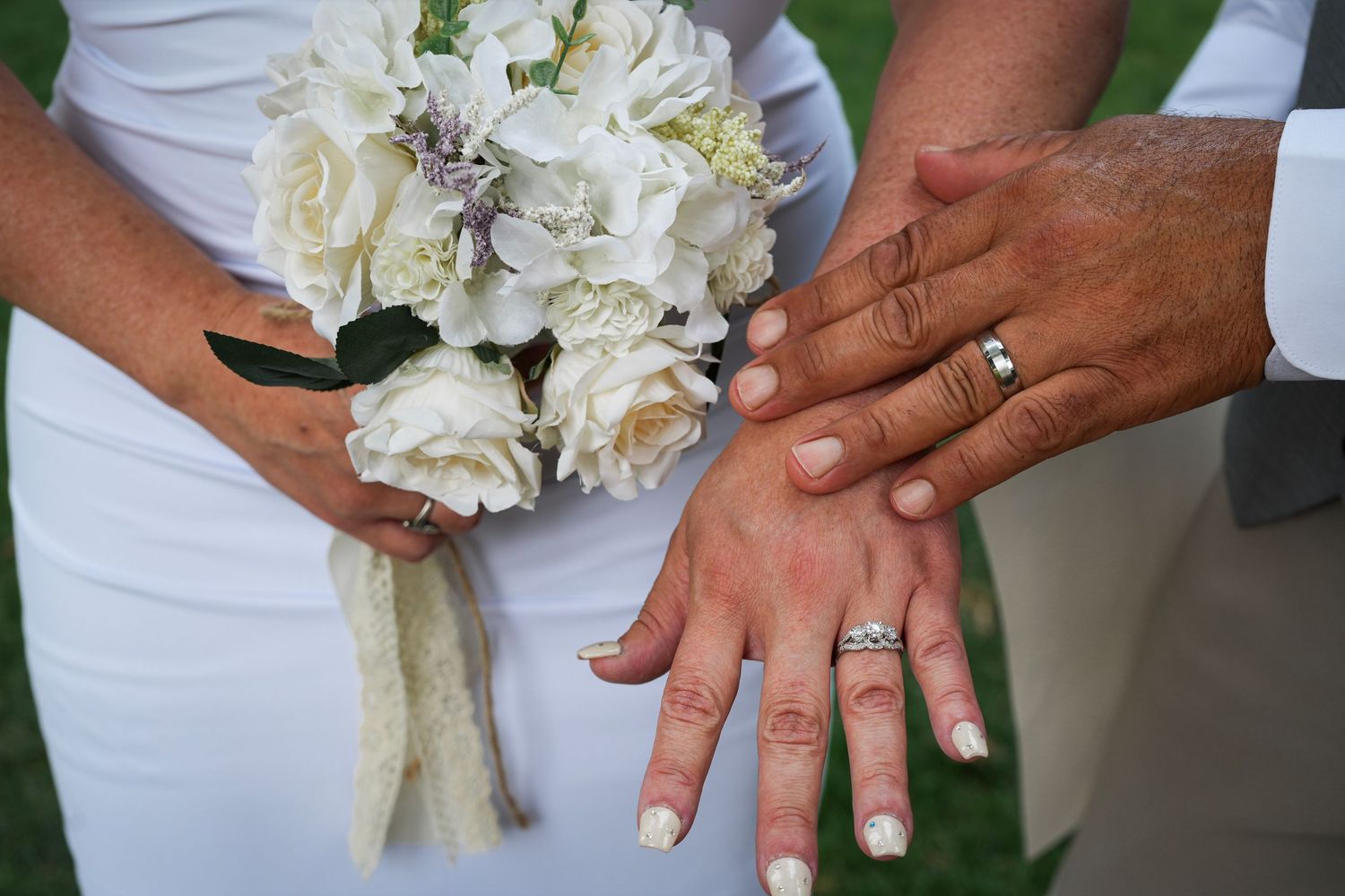 Close-up of newlyweds showing their wedding rings beside a white bridal bouquet.