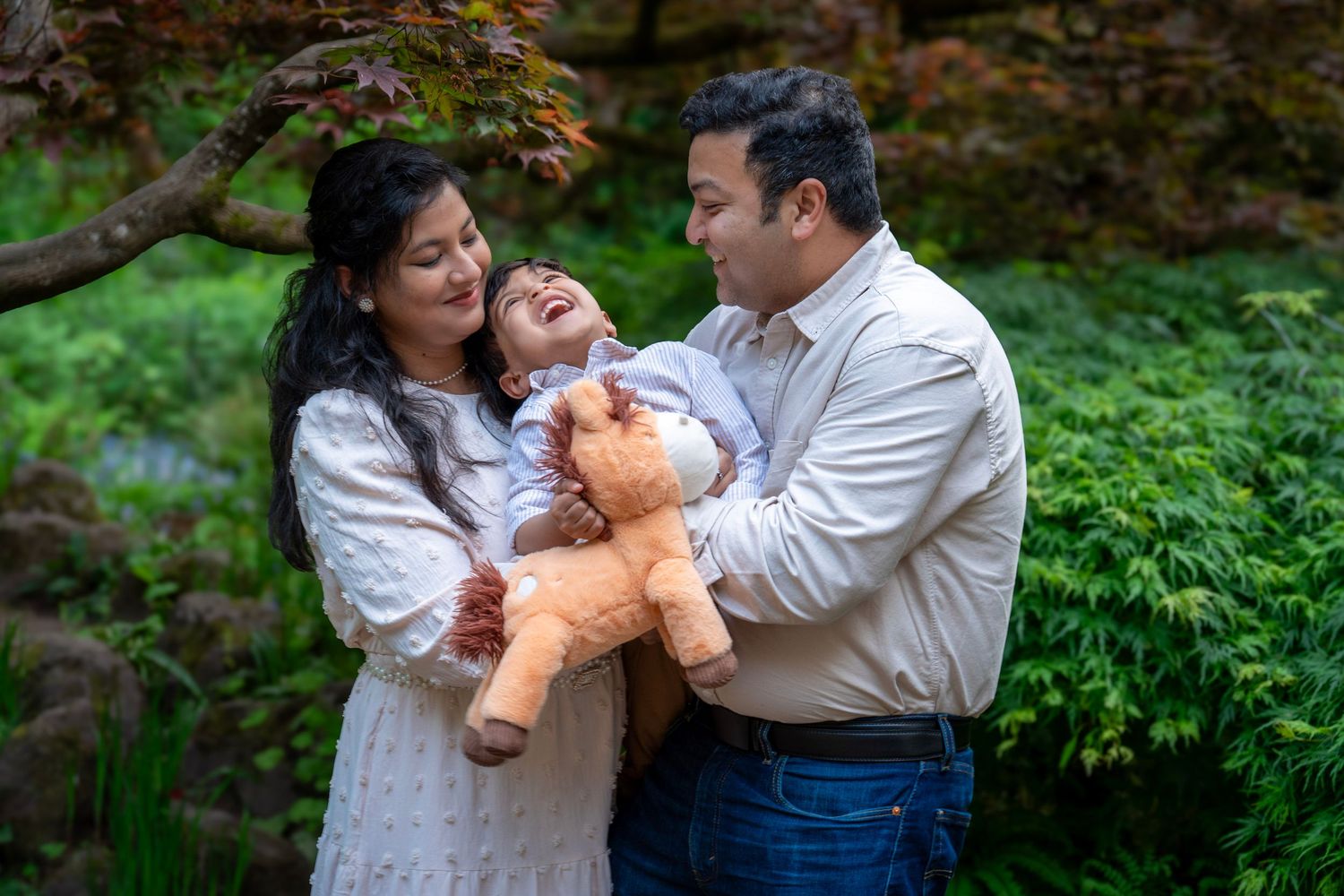 Mom and dad laughing with their baby during an outdoor family photography session surrounded by lush greenery