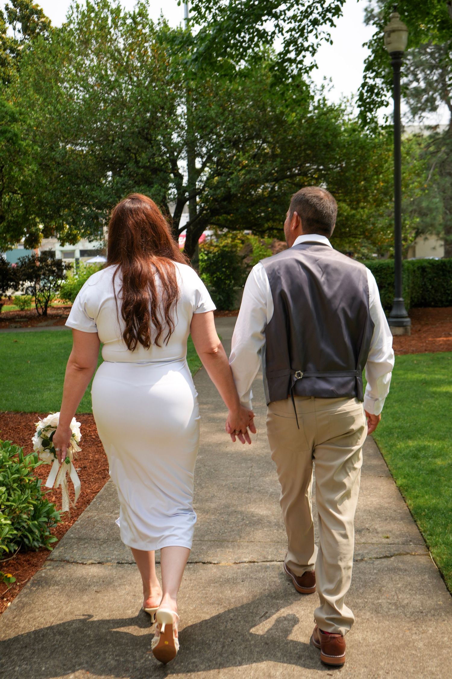 Bride and groom walking hand in hand through a garden after their courthouse wedding.