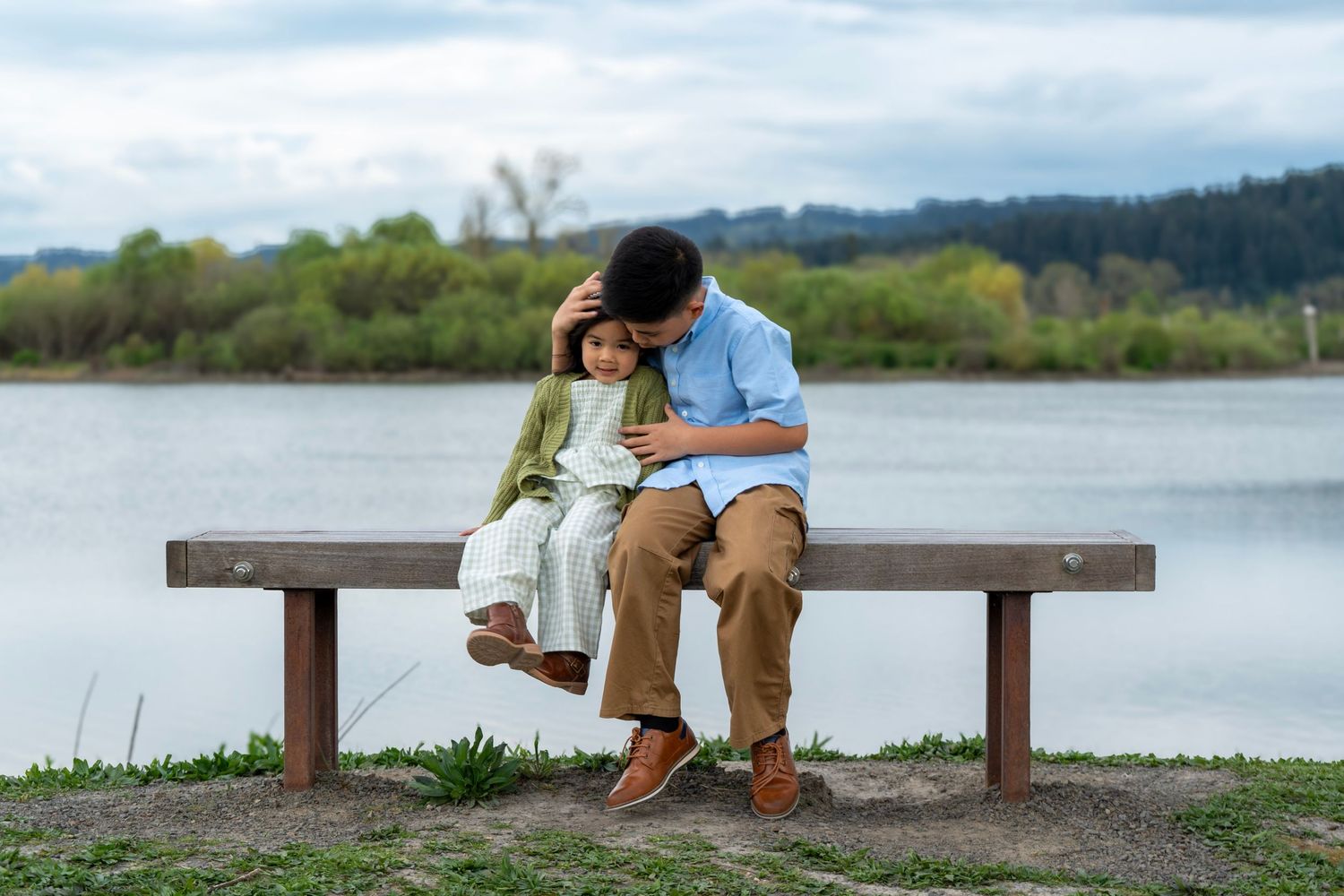 Brother and younger sister sharing a quiet moment together on a bench beside an Oregon lake