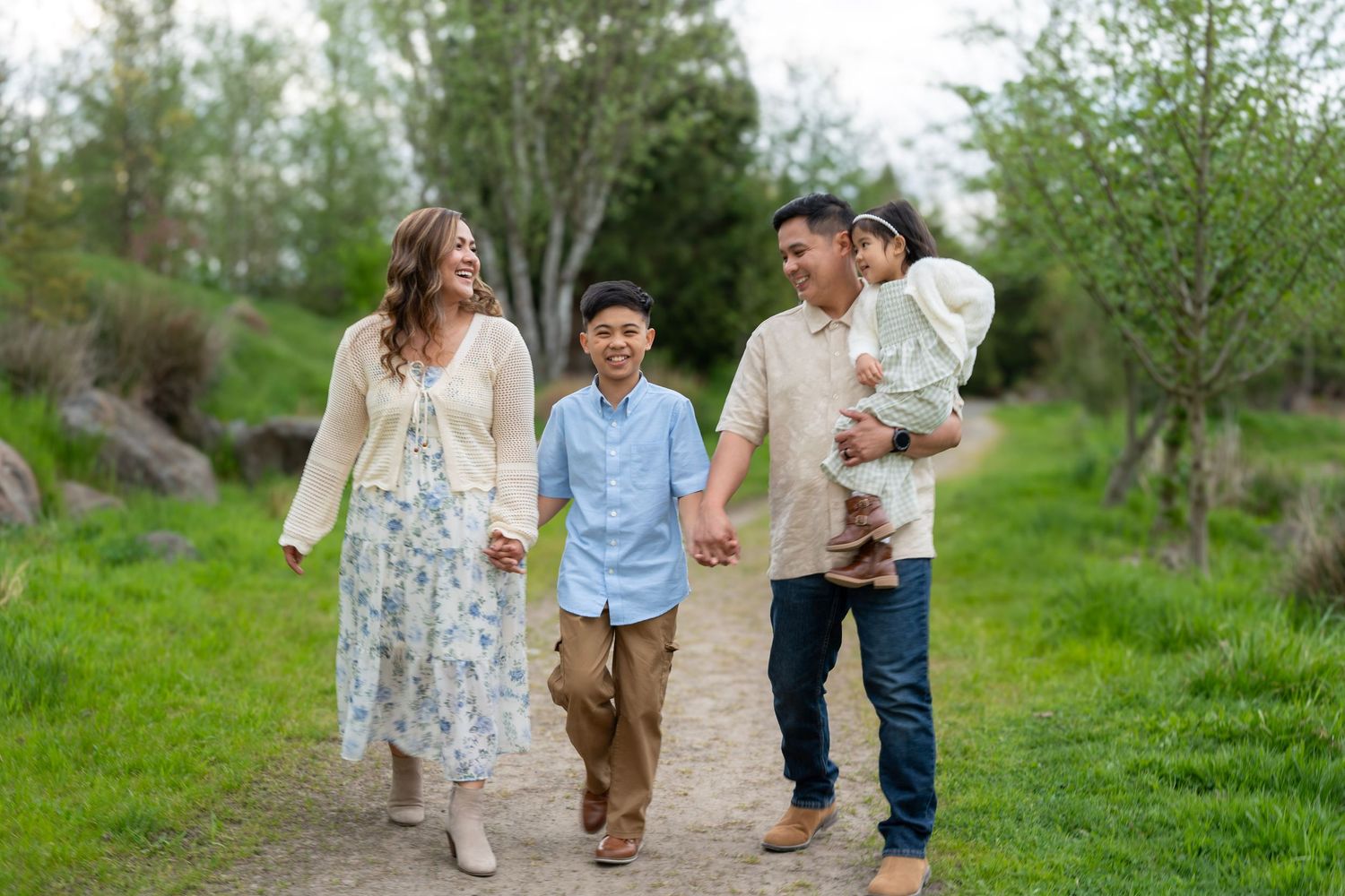 Family of four holding hands and walking together along a green trail during an outdoor family photography session