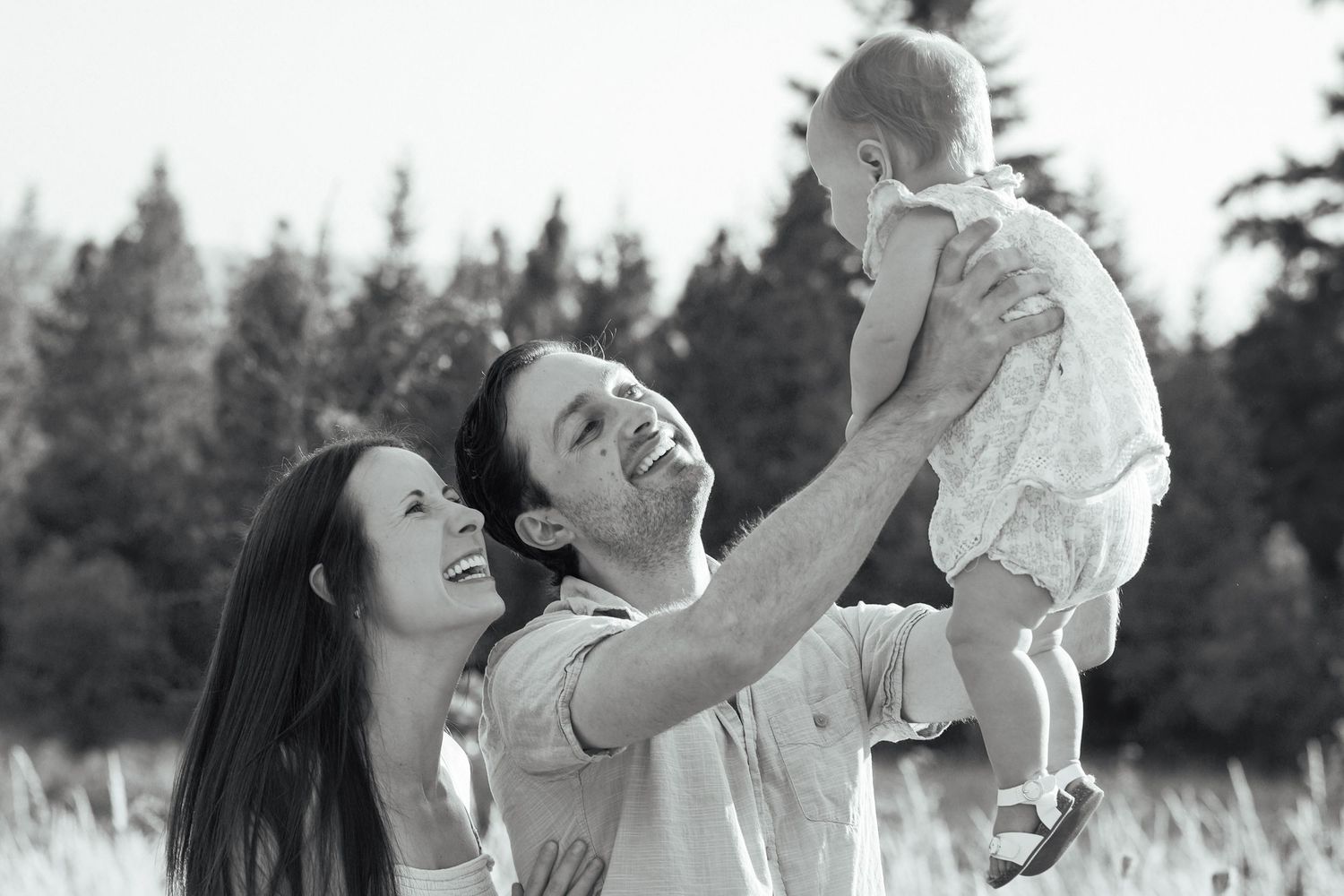 Mom and dad laughing as they lift their young daughter into the air during an outdoor family photography session