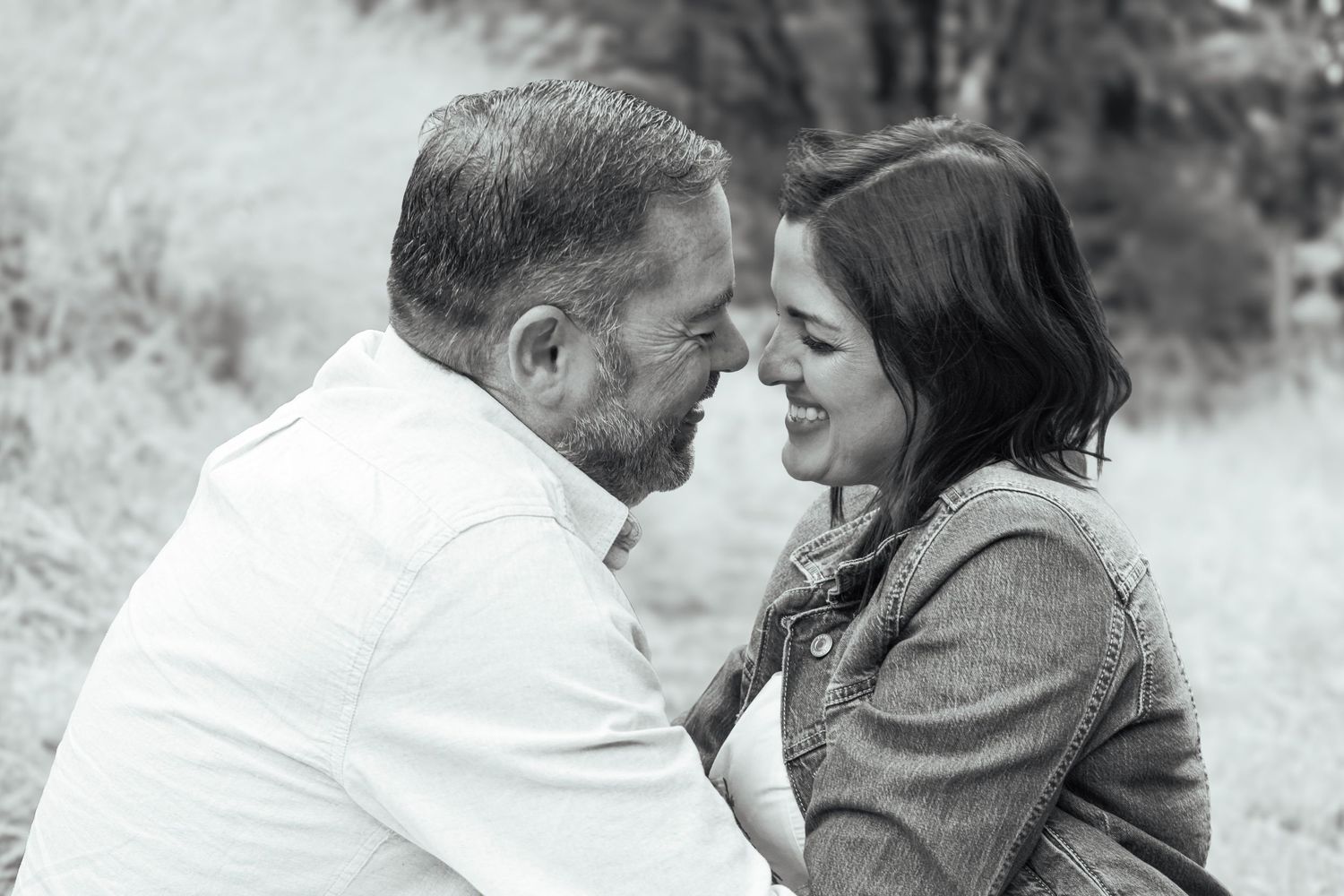 Black-and-white portrait of a smiling couple leaning close together during an outdoor photography session.