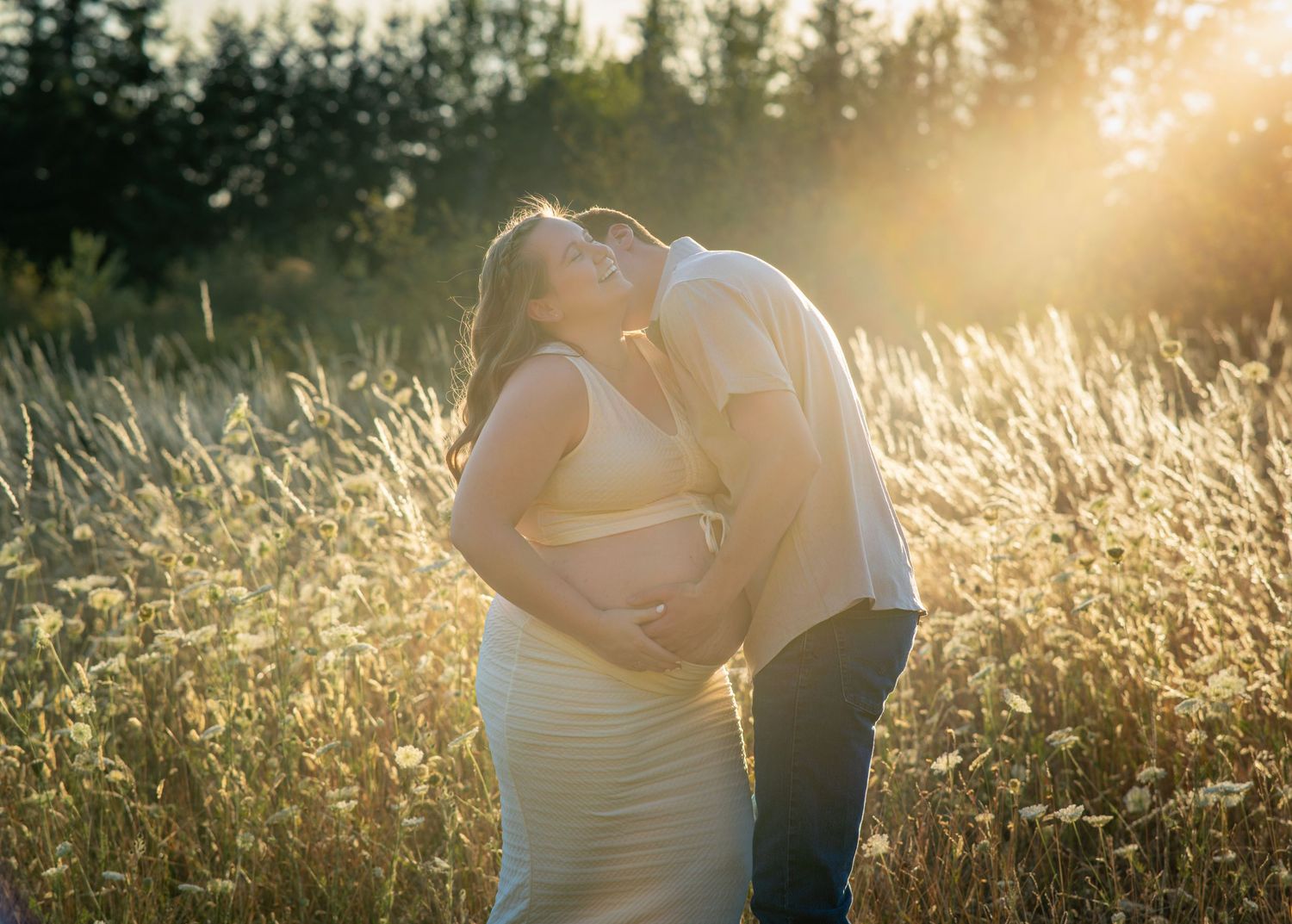 Expectant couple laughing and embracing in a golden field during an outdoor maternity photography session near Portland, Oregon