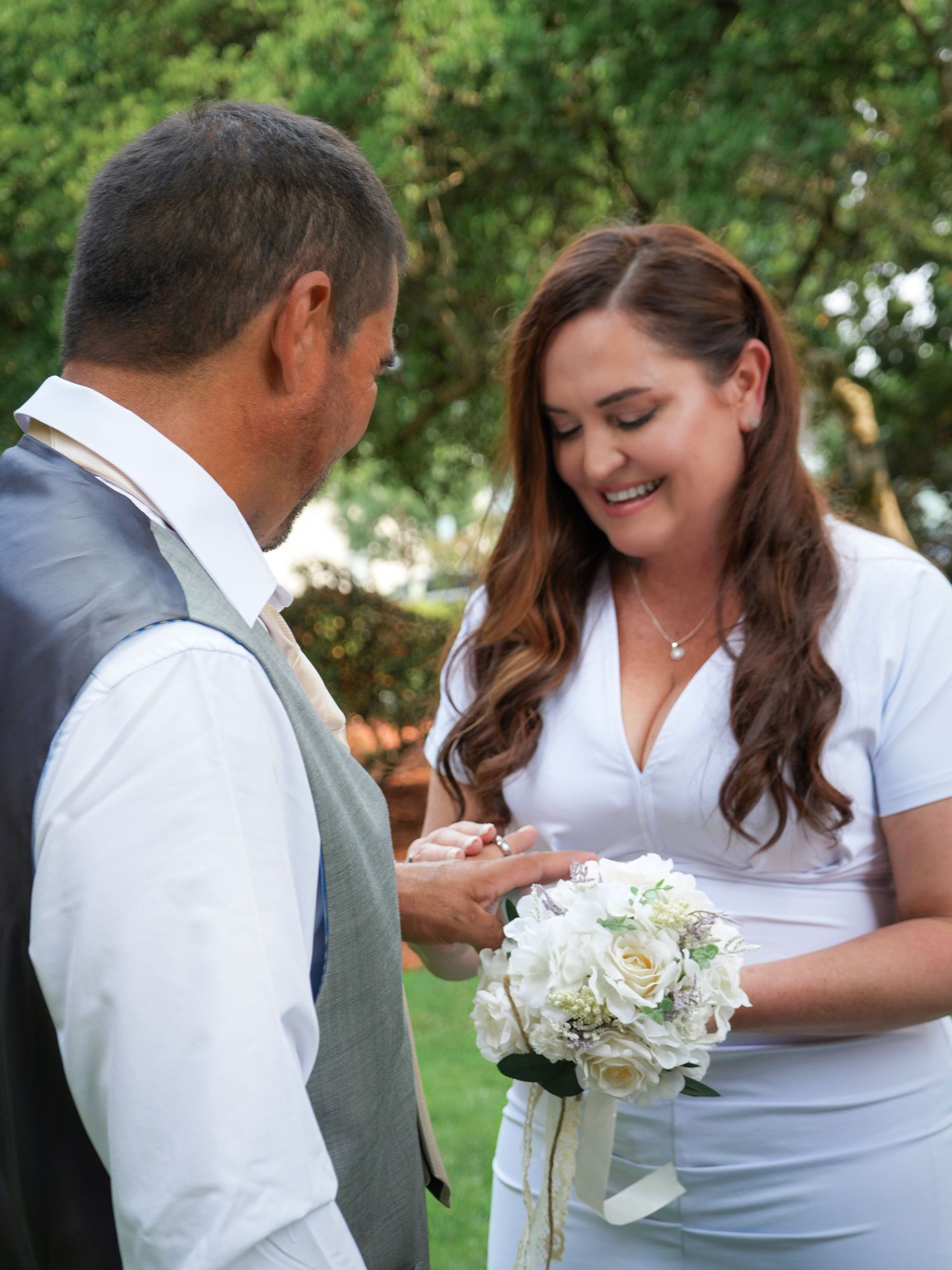 Bride smiling down at her wedding ring while holding a white flower bouquet.