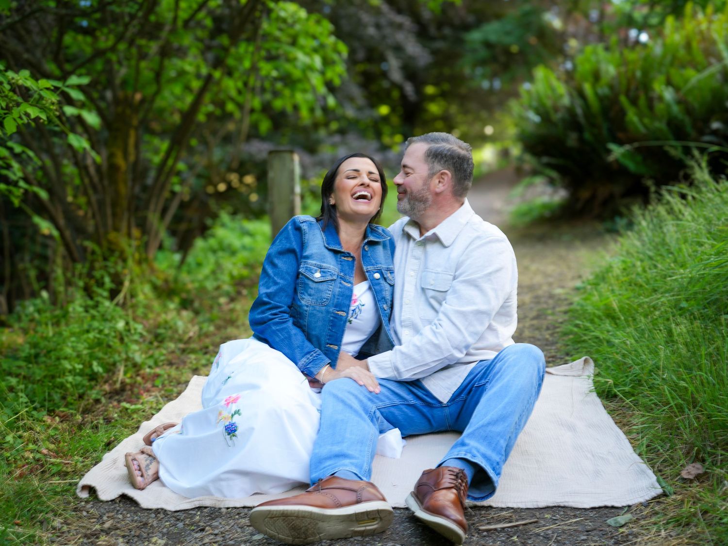 Couple sitting together on a blanket and laughing during a relaxed outdoor couples photography session