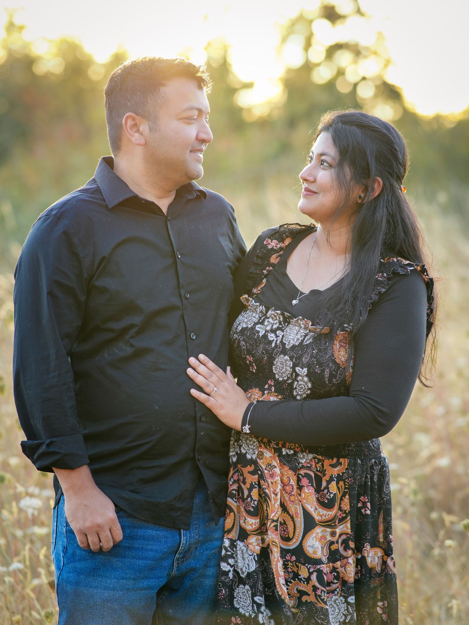 Couple smiling at each other while standing together in warm evening light during an outdoor photography session