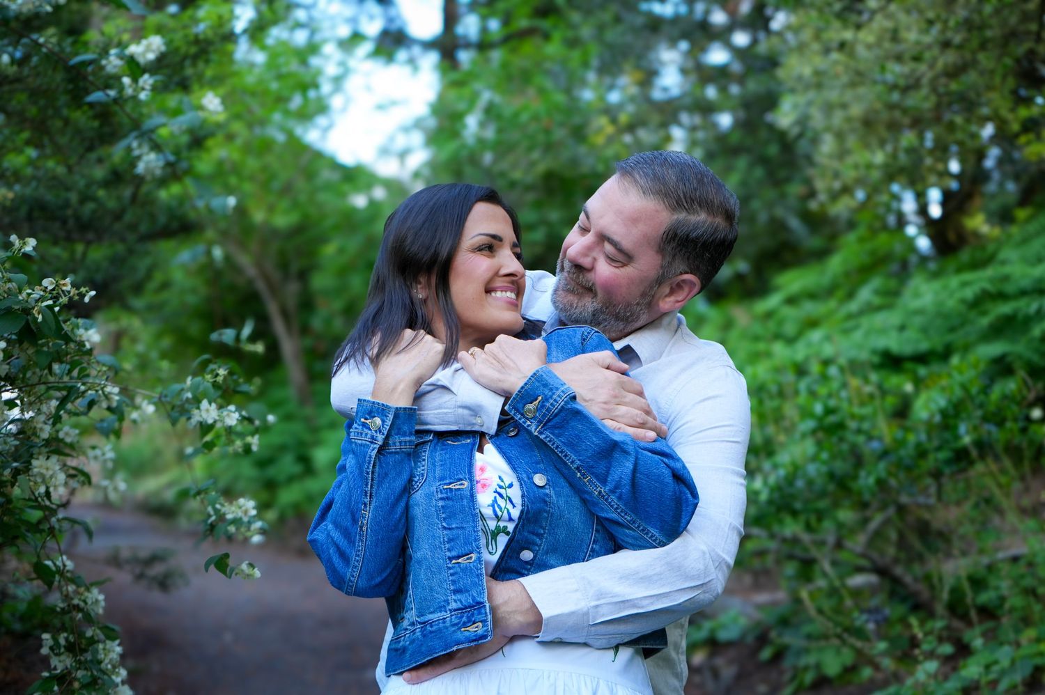 Couple smiling and cuddling together surrounded by lush greenery during an outdoor couples photography session
