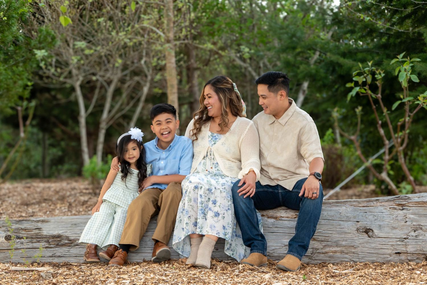 Family of four laughing together while sitting on a fallen log during a relaxed outdoor family photography session