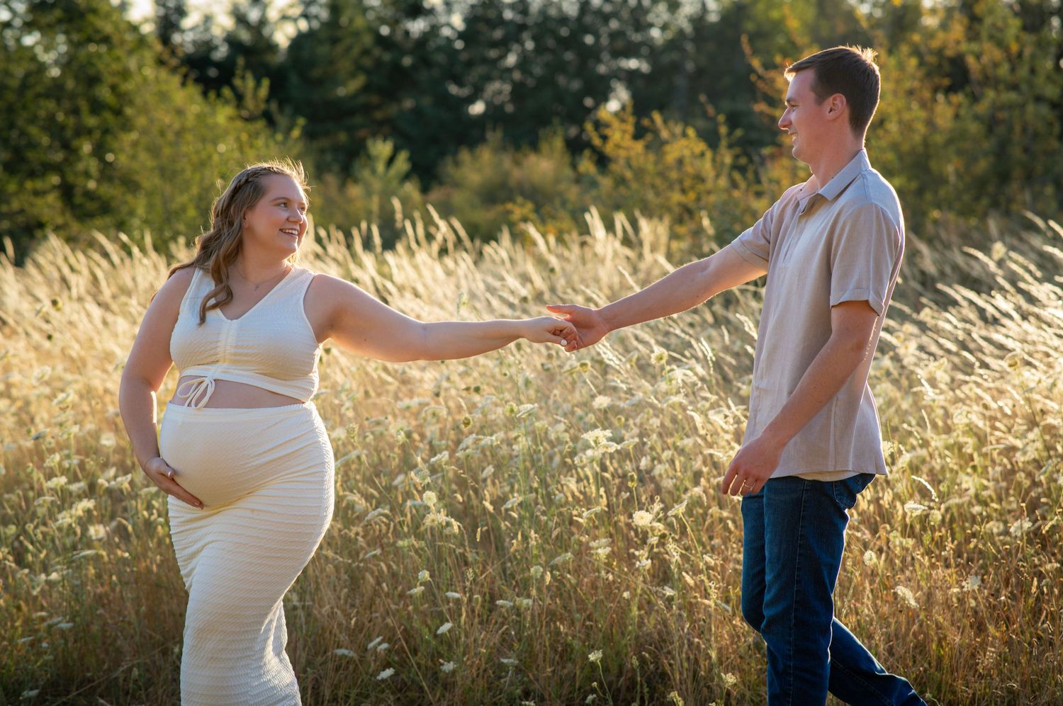 Expectant couple holding hands in a sunlit field during an outdoor maternity photography session near Beaverton, Oregon