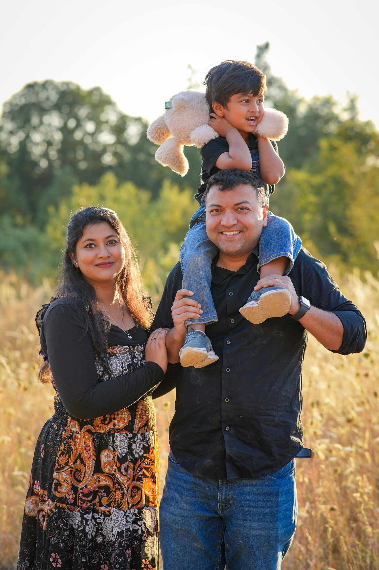 Family smiling together as a young boy rides on his dad's shoulders during a golden hour family session