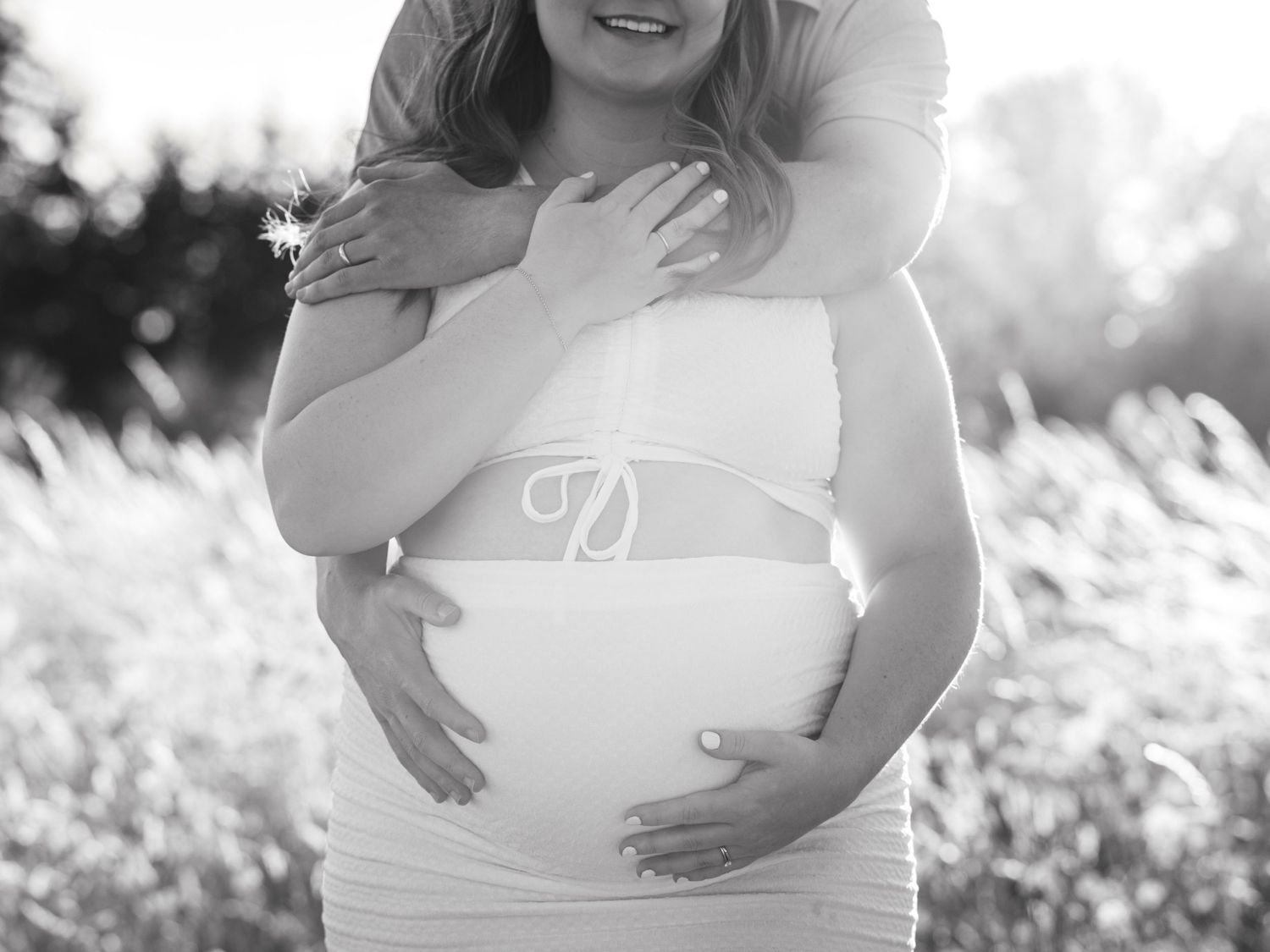 Expectant couple embracing and cradling her baby bump during an outdoor maternity photography session at sunset