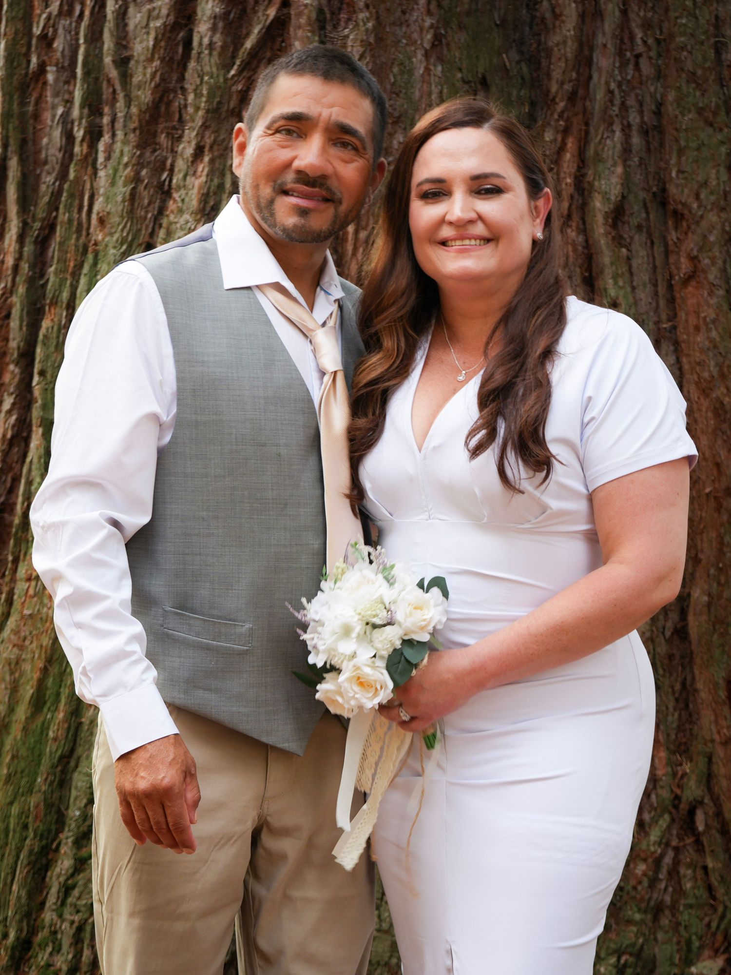 Newlywed couple smiling together beside a large tree after their courthouse wedding.