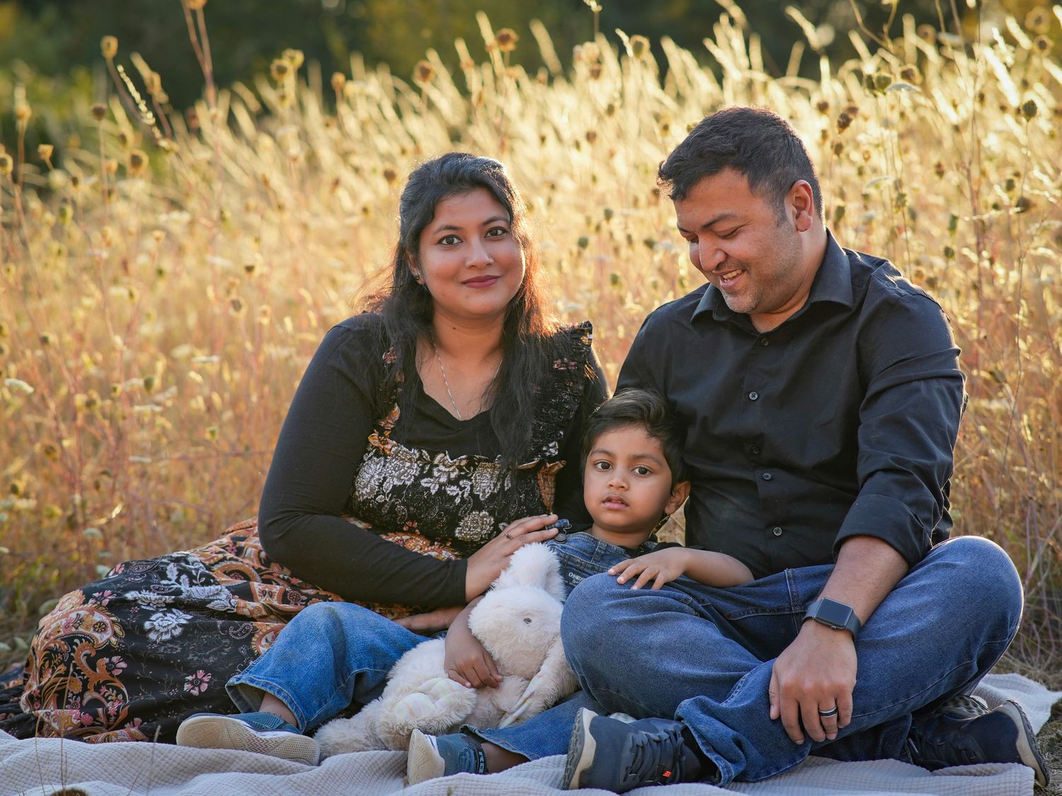 Family of three cuddling together on a blanket in a golden field during an outdoor family photography session