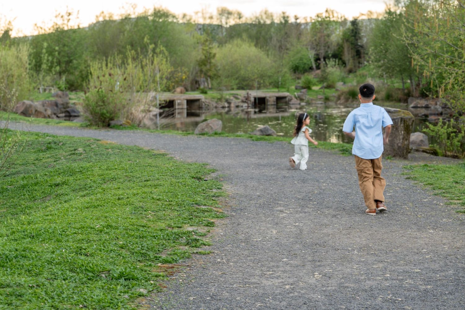 Brother and sister running along a path beside a pond during an outdoor family photography session.