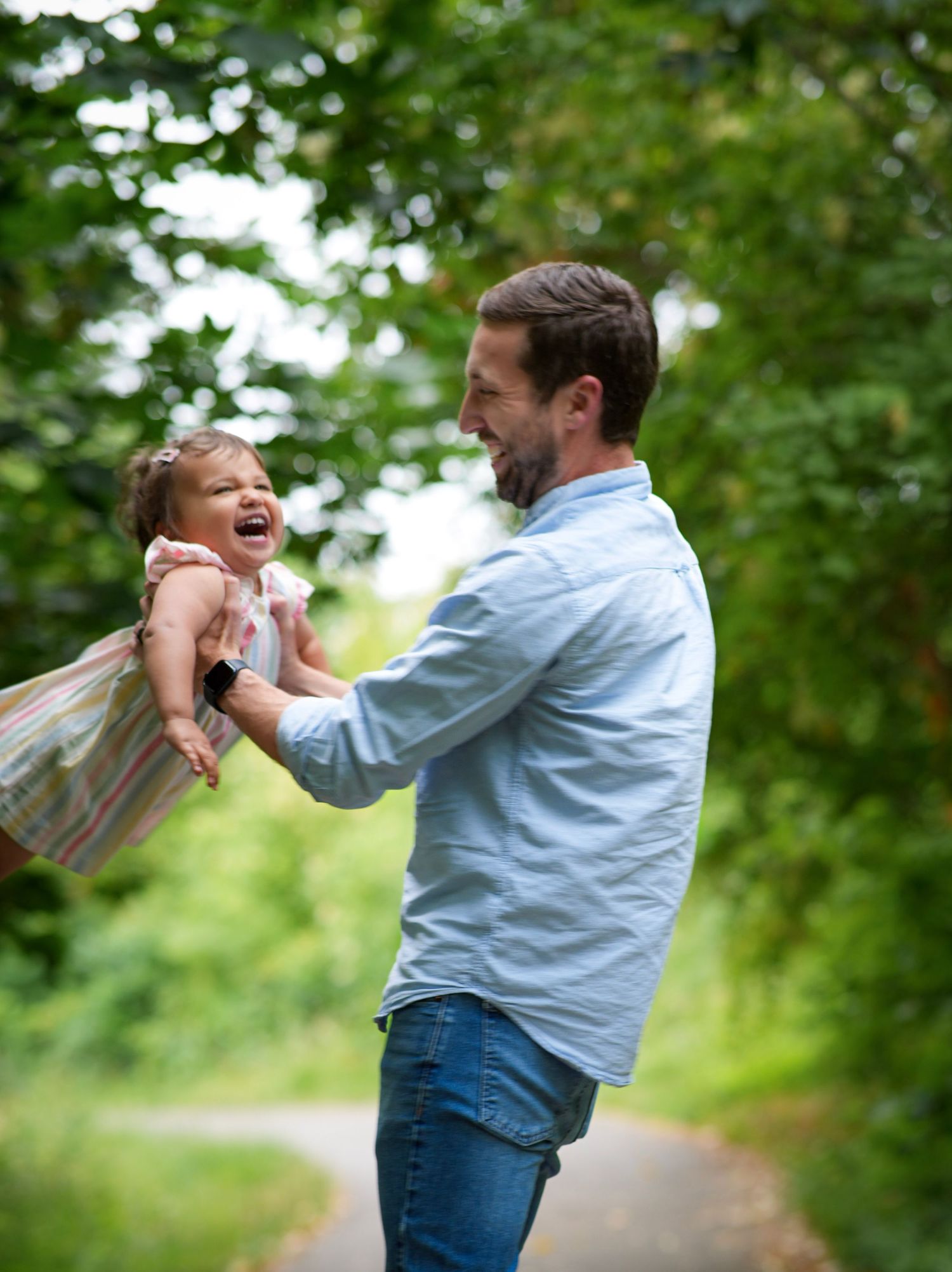 Dad laughing and swinging his toddler daughter during a playful outdoor family photography session
