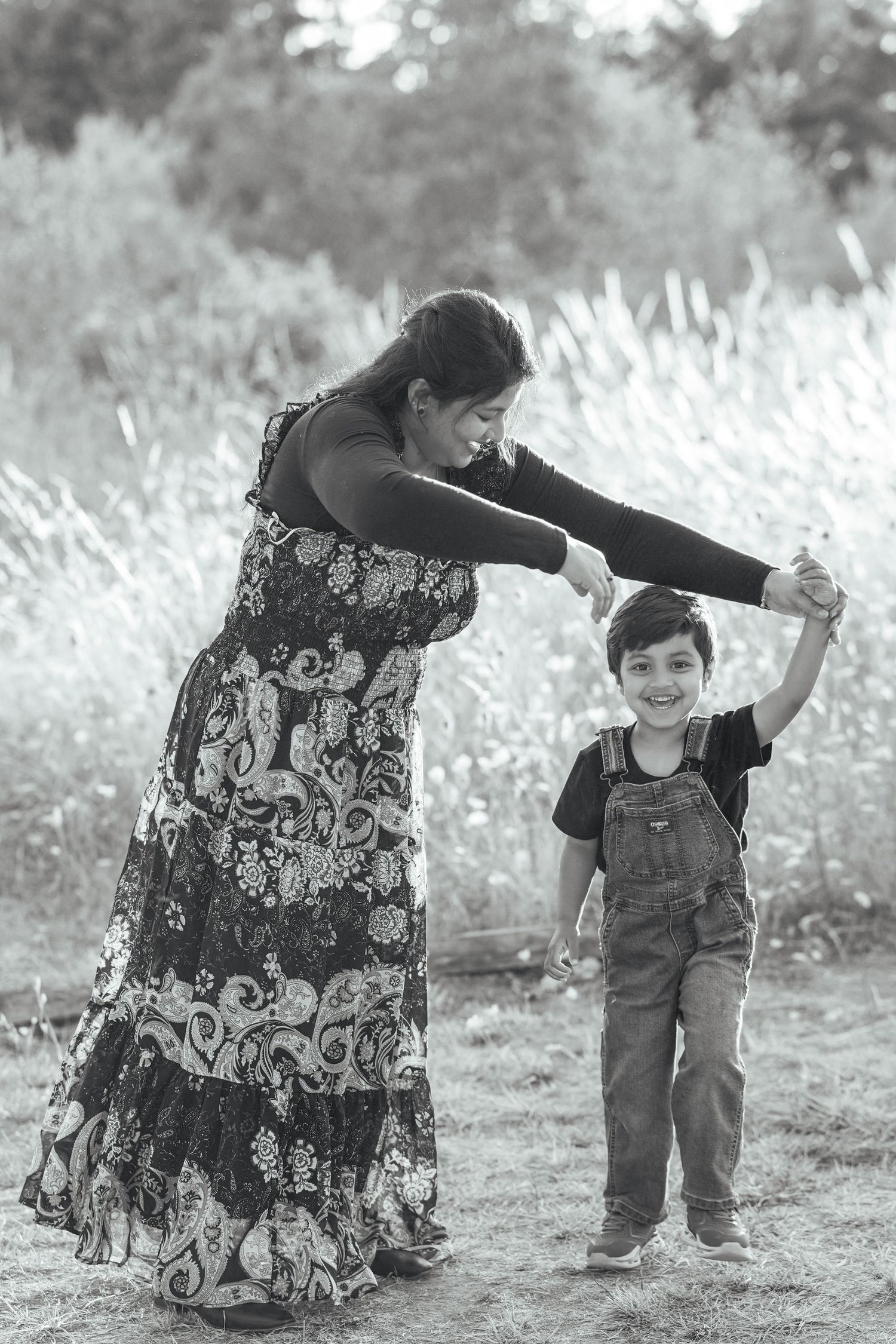 Mom smiling down at her young son as they hold hands and play together during an outdoor family photography session