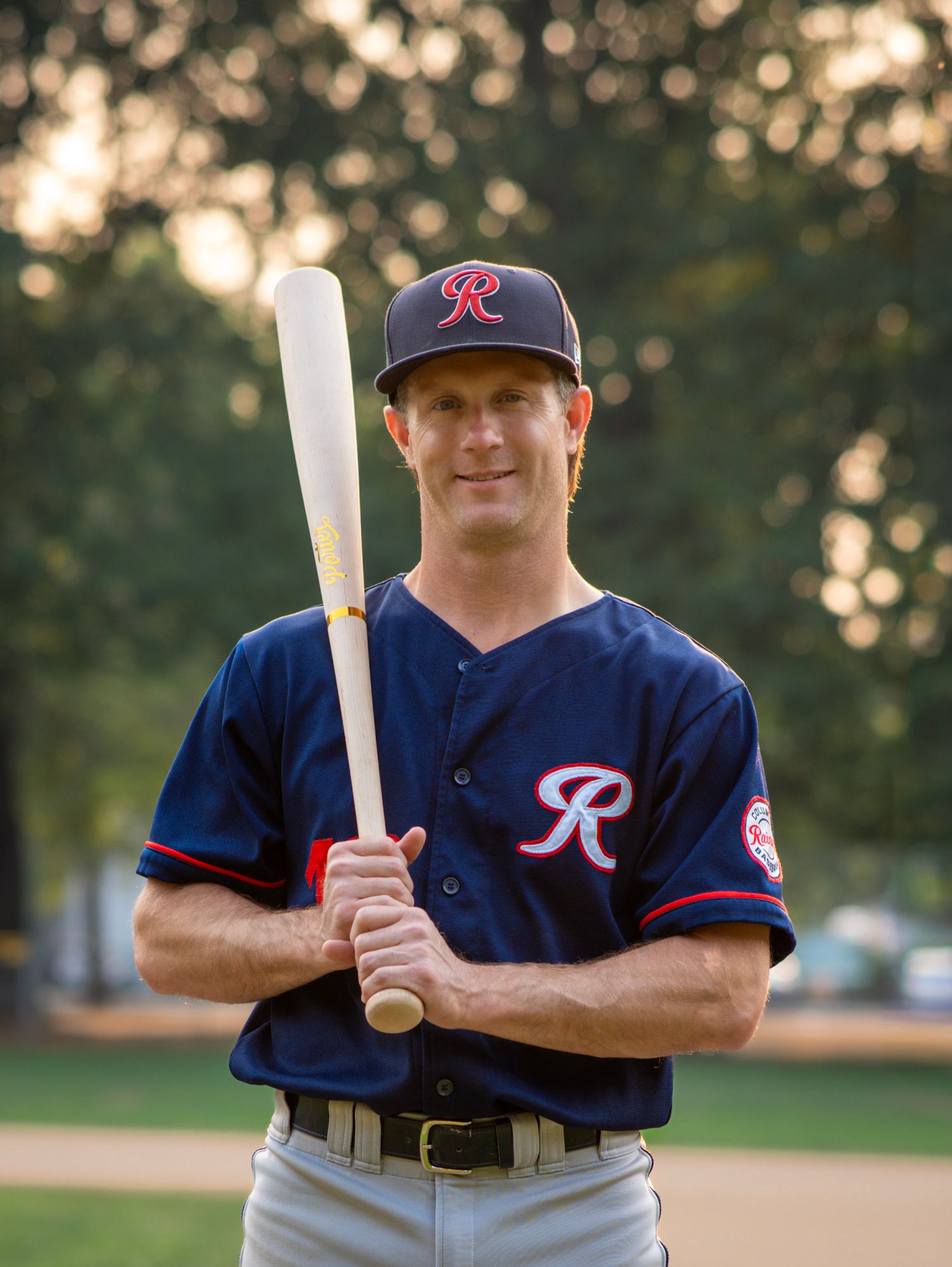 Baseball player holding a bat upright for an individual sports portrait on the field.