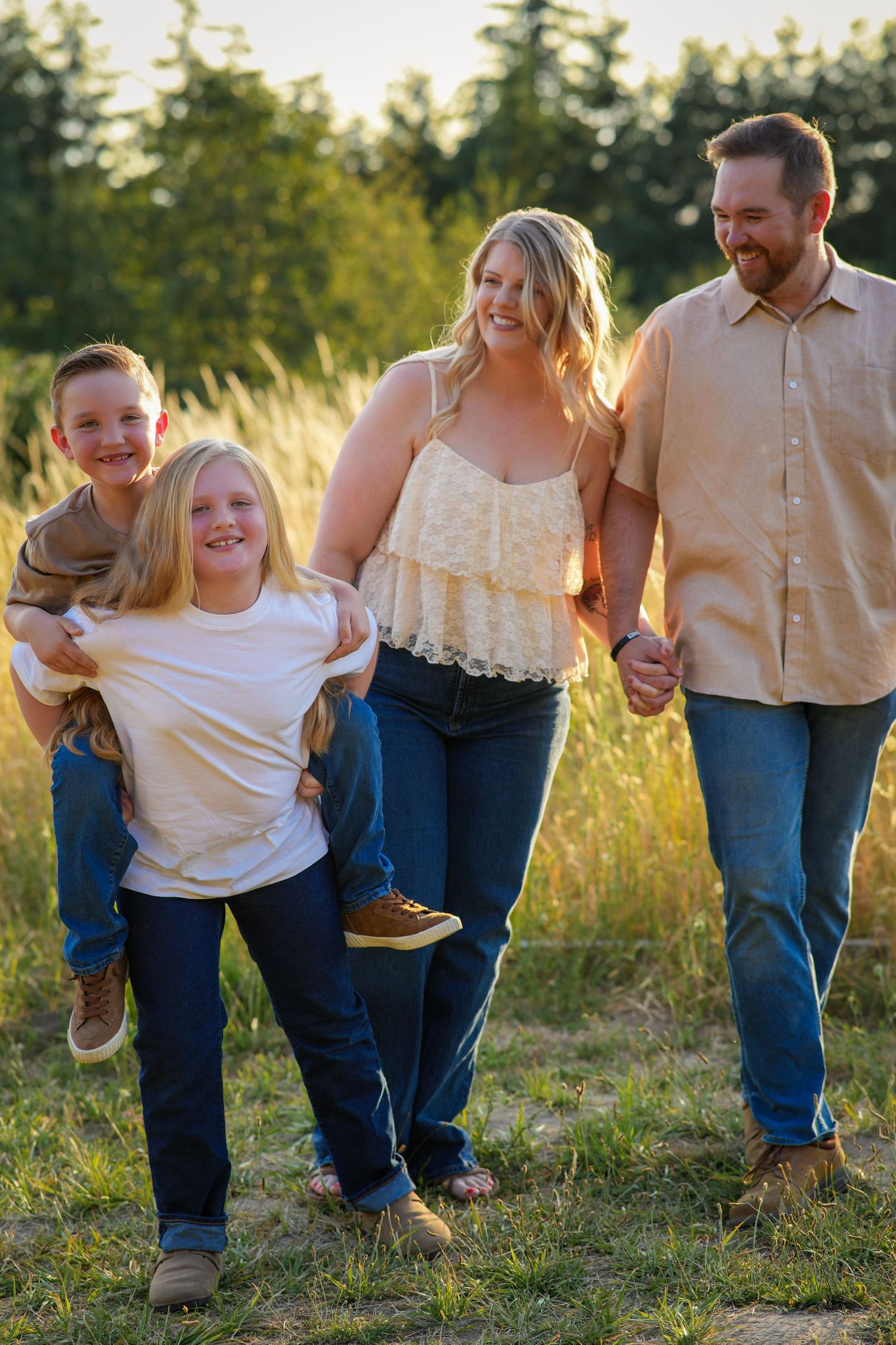 Family of four laughing and walking together through a golden field during an outdoor family photography session