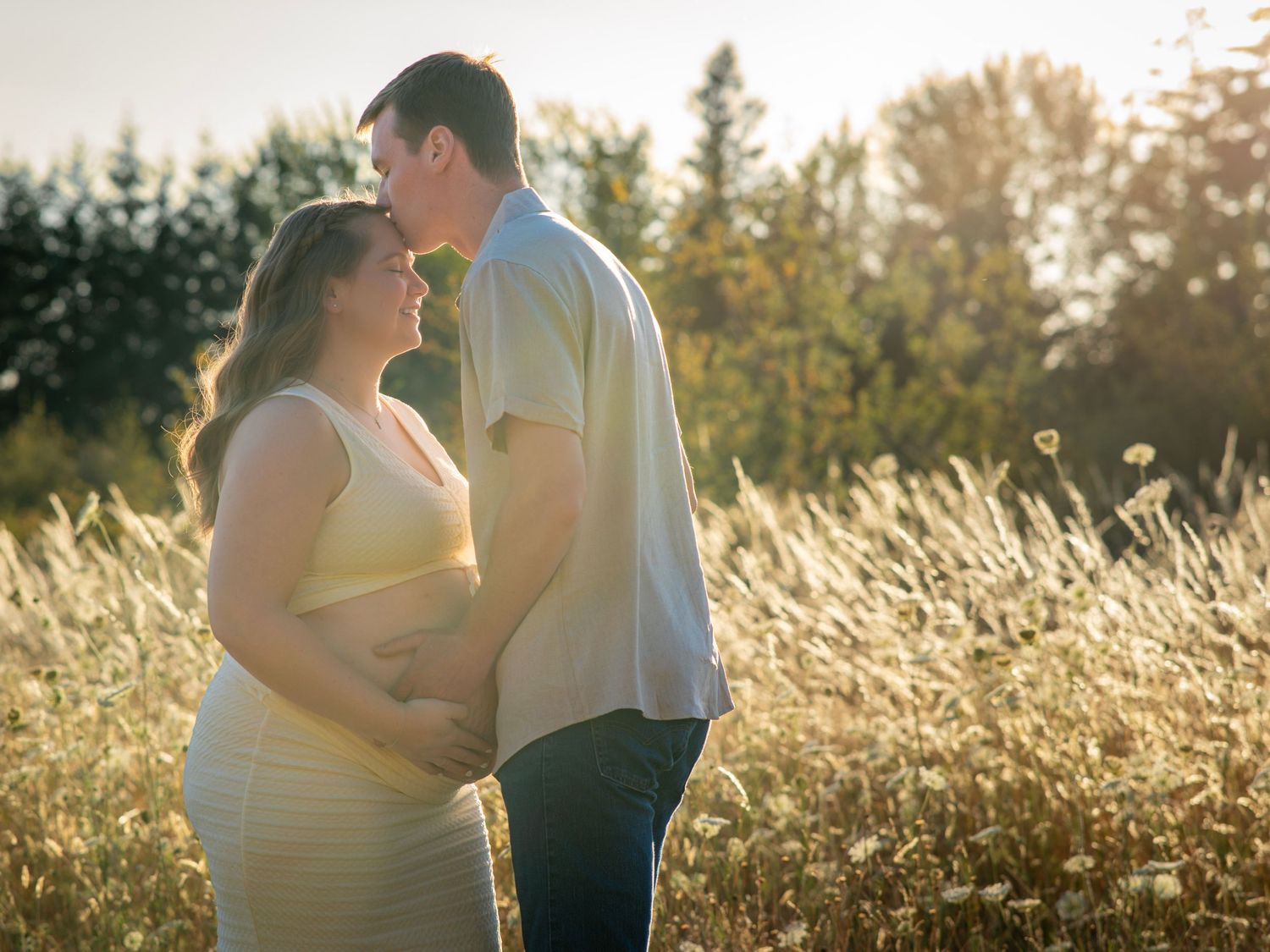 Expectant father kissing his partner's forehead as they cradle her baby bump during a golden hour maternity session