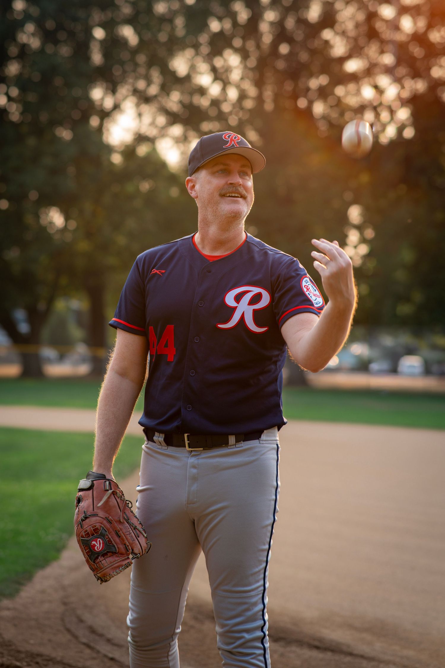 Baseball player tossing a ball in the air while holding his glove during a golden hour portrait session.