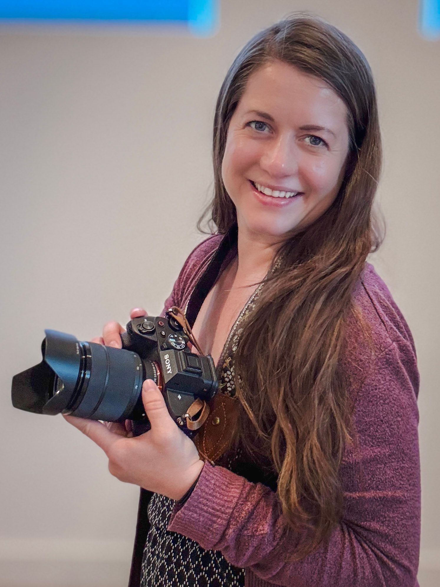 Kate Vargas smiling while holding a Sony camera, portrait photographer and owner of Kate Vargas Photography.
