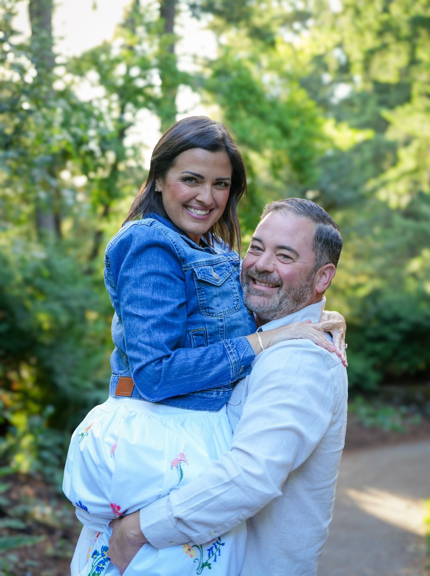 Smiling couple embracing as he lifts her during a romantic outdoor couples photography session in a garden