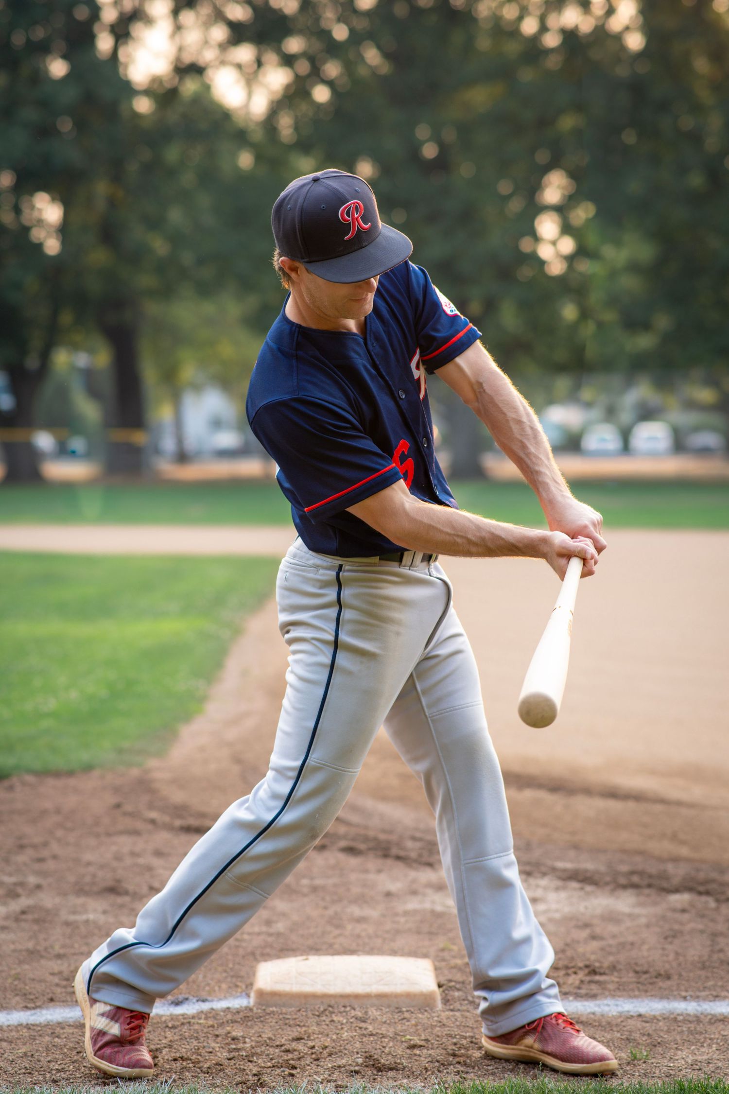 Baseball player swinging a bat at home plate during an evening sports photography session.