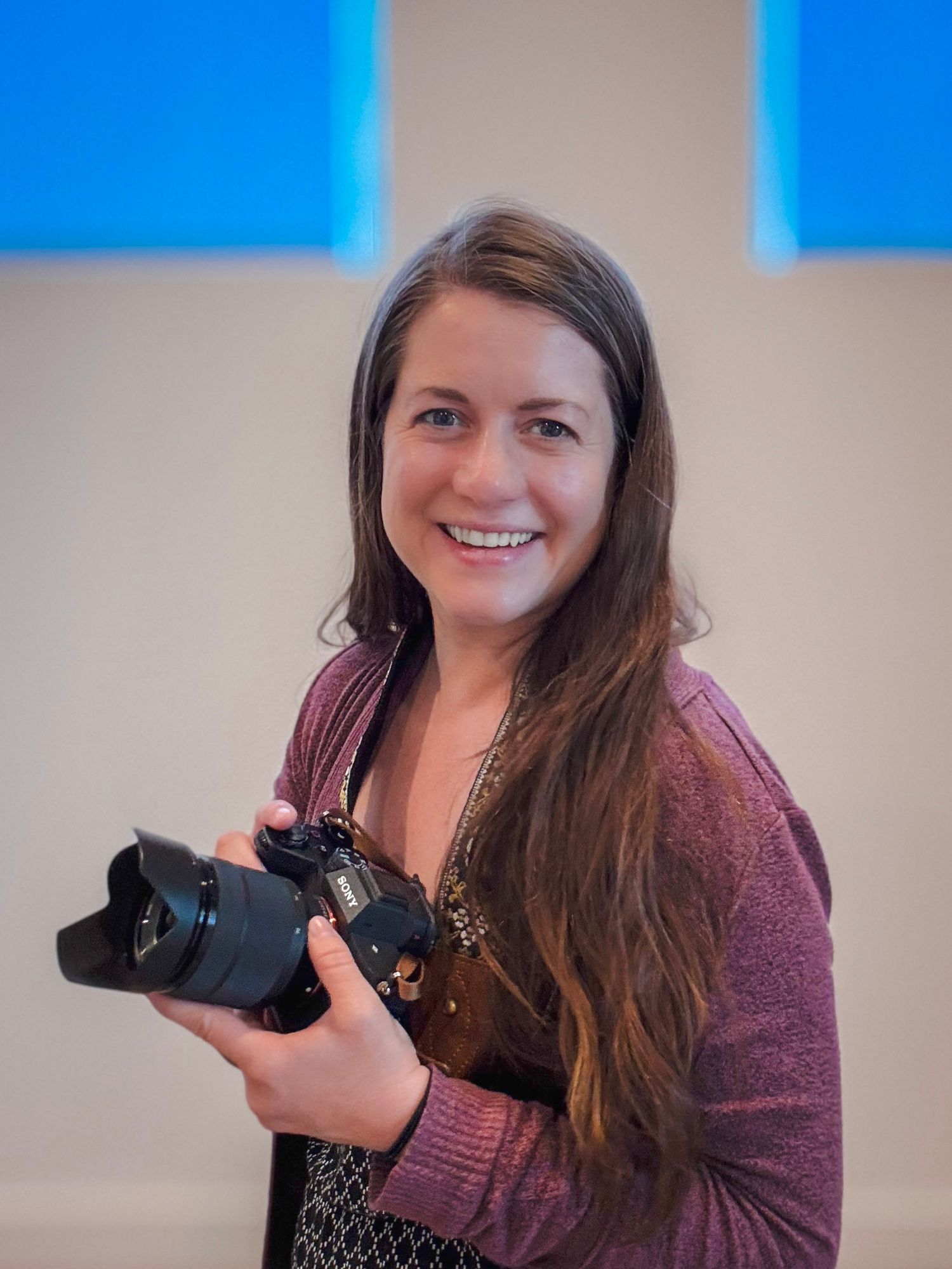Kate Vargas smiling while holding a Sony camera, portrait photographer and owner of Kate Vargas Photography.