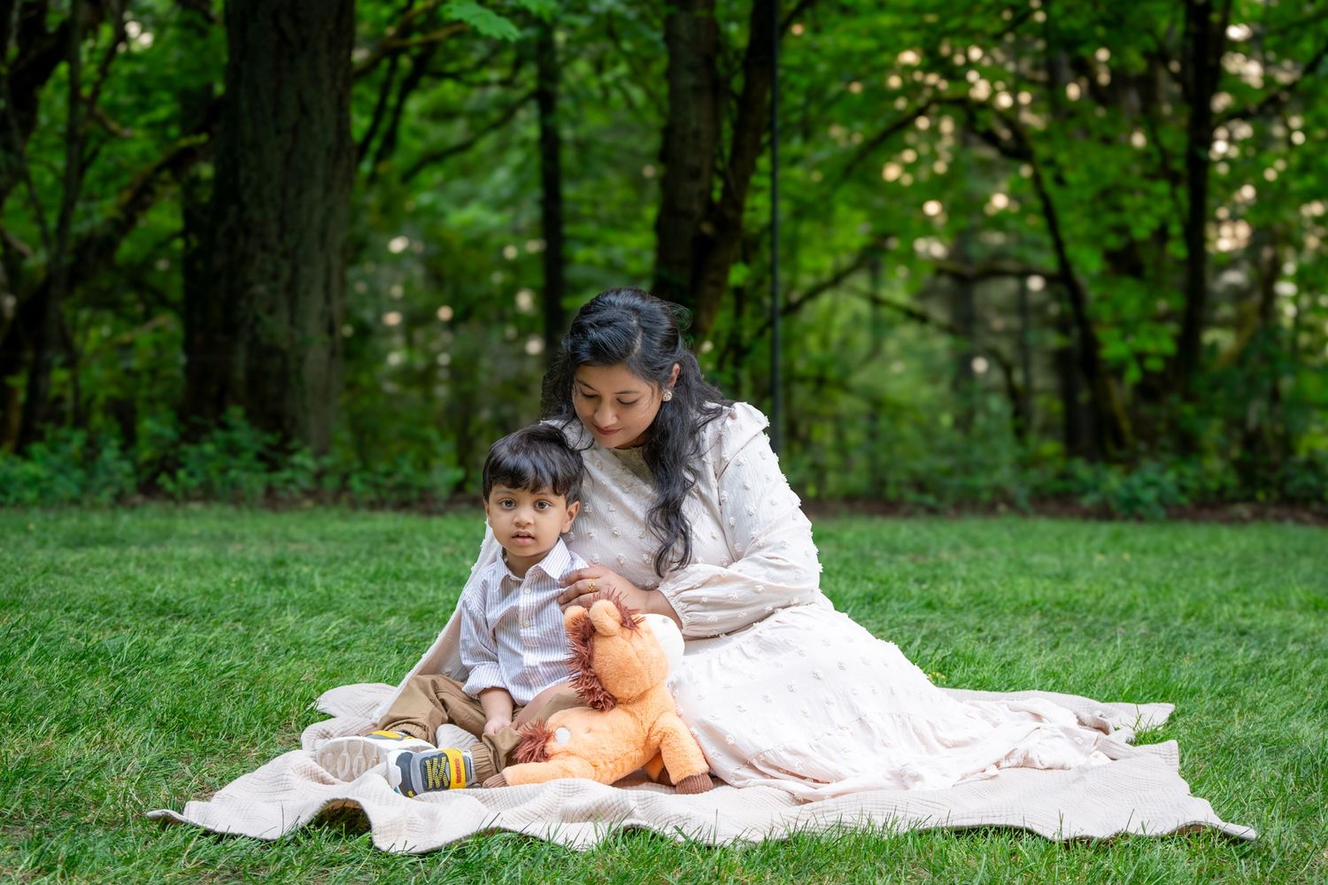 Mom cuddling her young son on a blanket beneath the trees during a relaxed outdoor family photography session