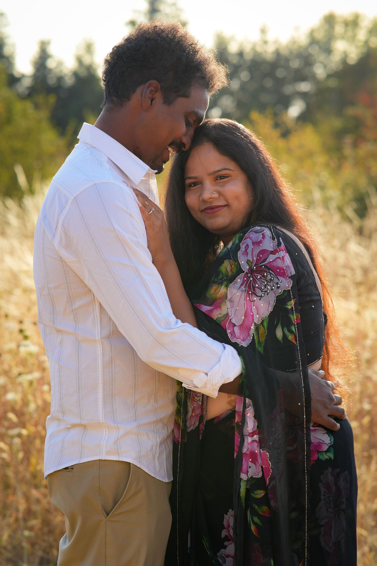 Couple cuddling together among glowing golden grasses during an outdoor sunset photography session