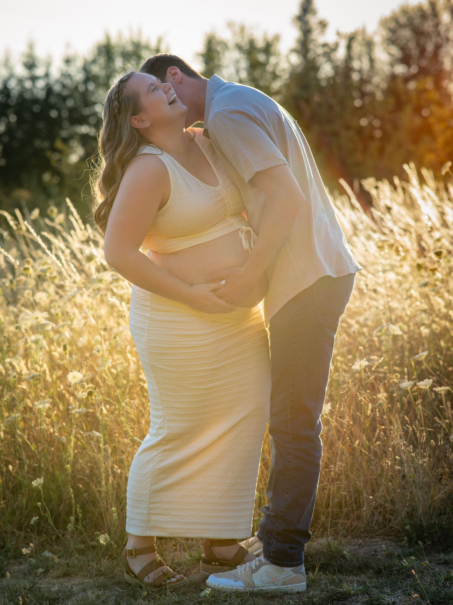 Couple embracing during a golden hour maternity session in a sunlit field.