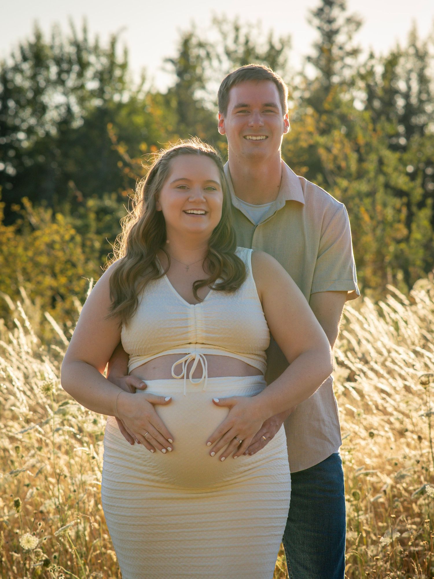 Expectant couple smiling together with their hands resting on the baby bump.