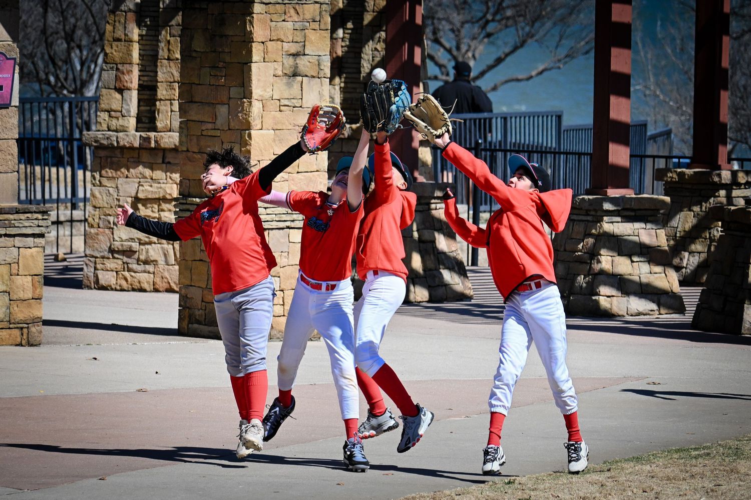 Three baseball players in red uniforms celebrate with gloves raised outside stadium entrance.