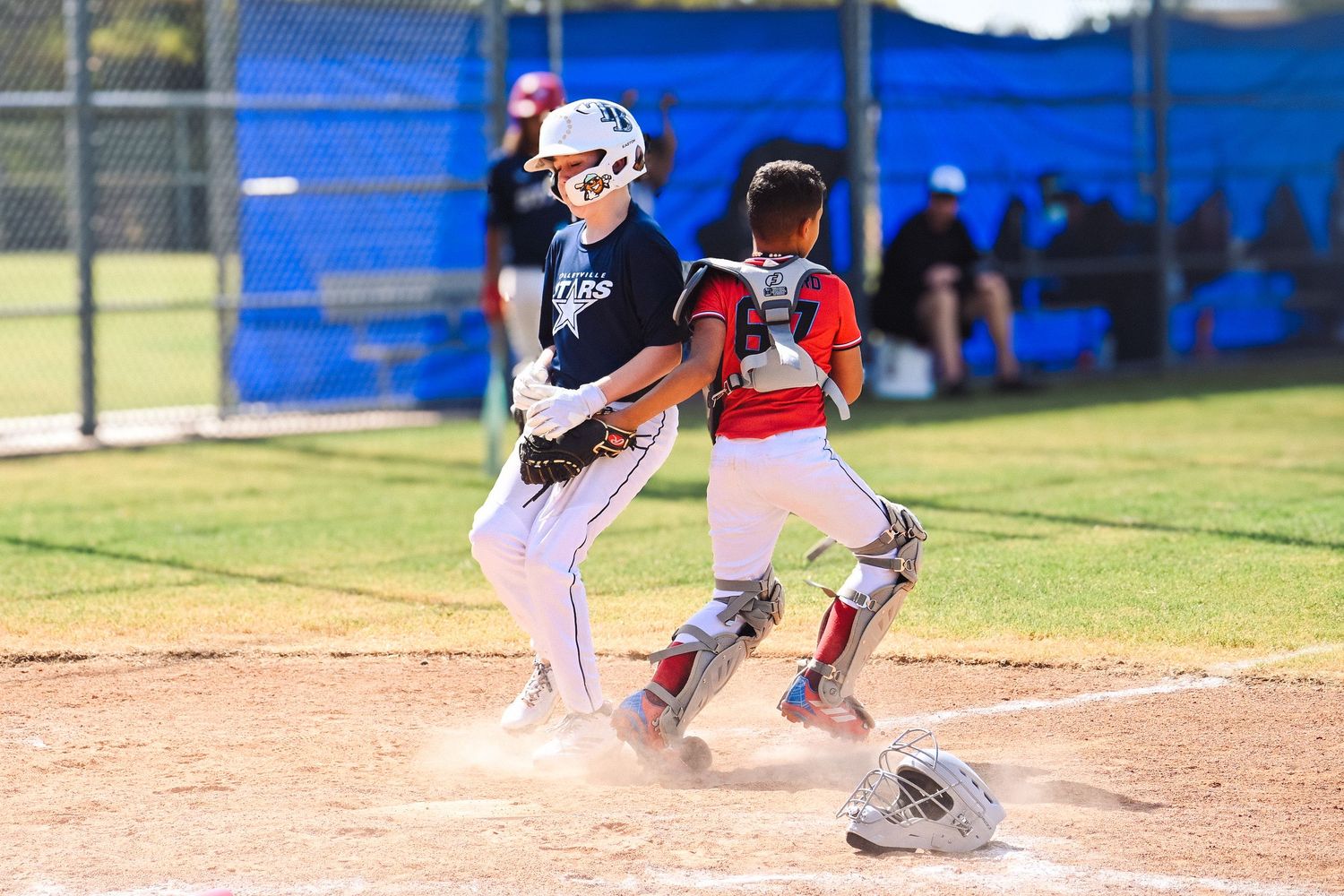 Youth baseball player slides into home plate as catcher waits during an exciting little league game.
