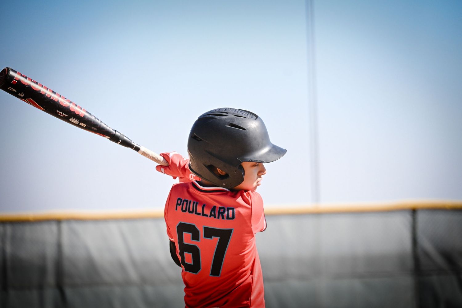Youth baseball player named Poullard number 67 in red uniform swinging bat during practice session.
