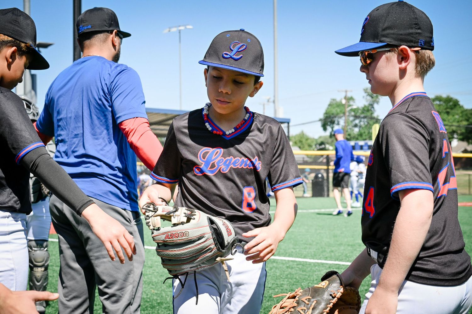 Young baseball players in Legends uniforms exchange handshakes on a sunny field after a youth baseball game.