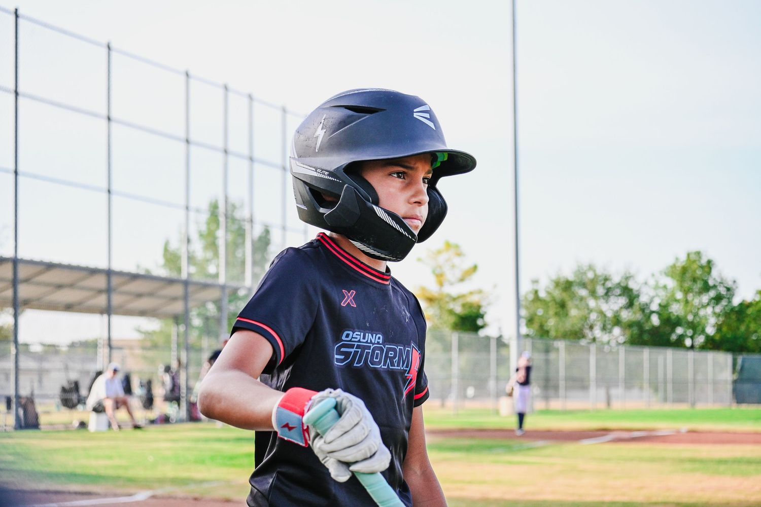 Young baseball player in black helmet and jersey holds a bat, ready to bat at an outdoor baseball field.