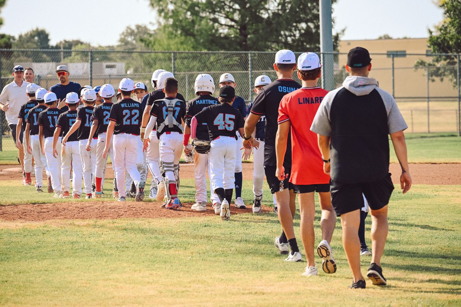 Youth baseball teams line up for post-game handshake on a sunny baseball field after a game.
