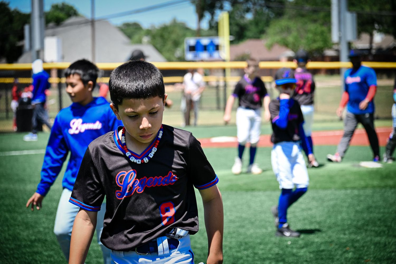 Young baseball player in black jersey walks on green field during youth baseball game outdoors.