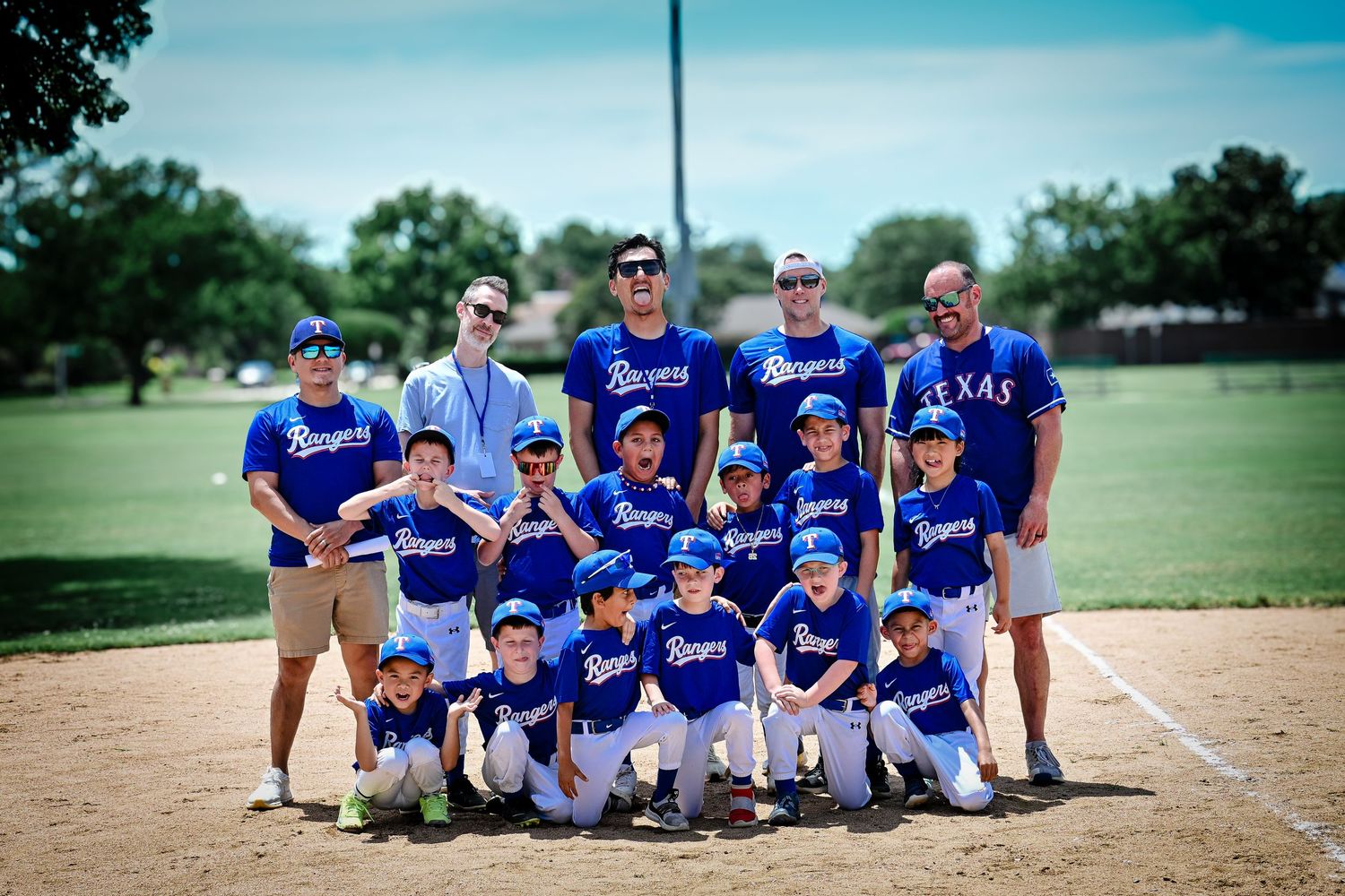 Little league Rangers baseball team posing for group photo with coaches on baseball diamond.