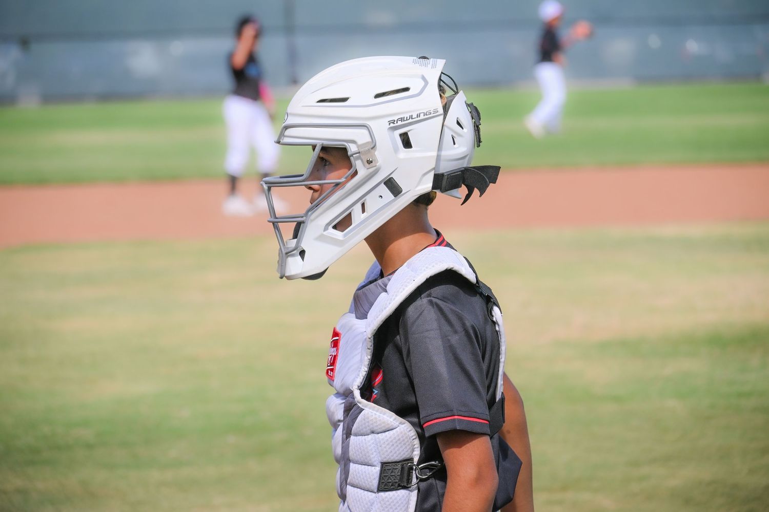 Young baseball catcher wearing full protective gear helmet and chest protector on field.