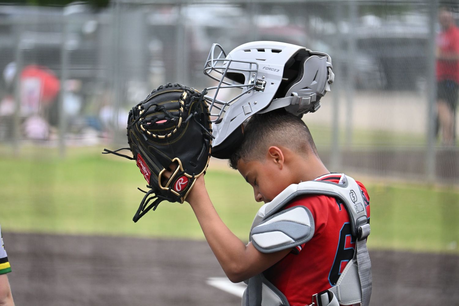 Youth baseball catcher adjusting helmet with catcher's mitt at game.